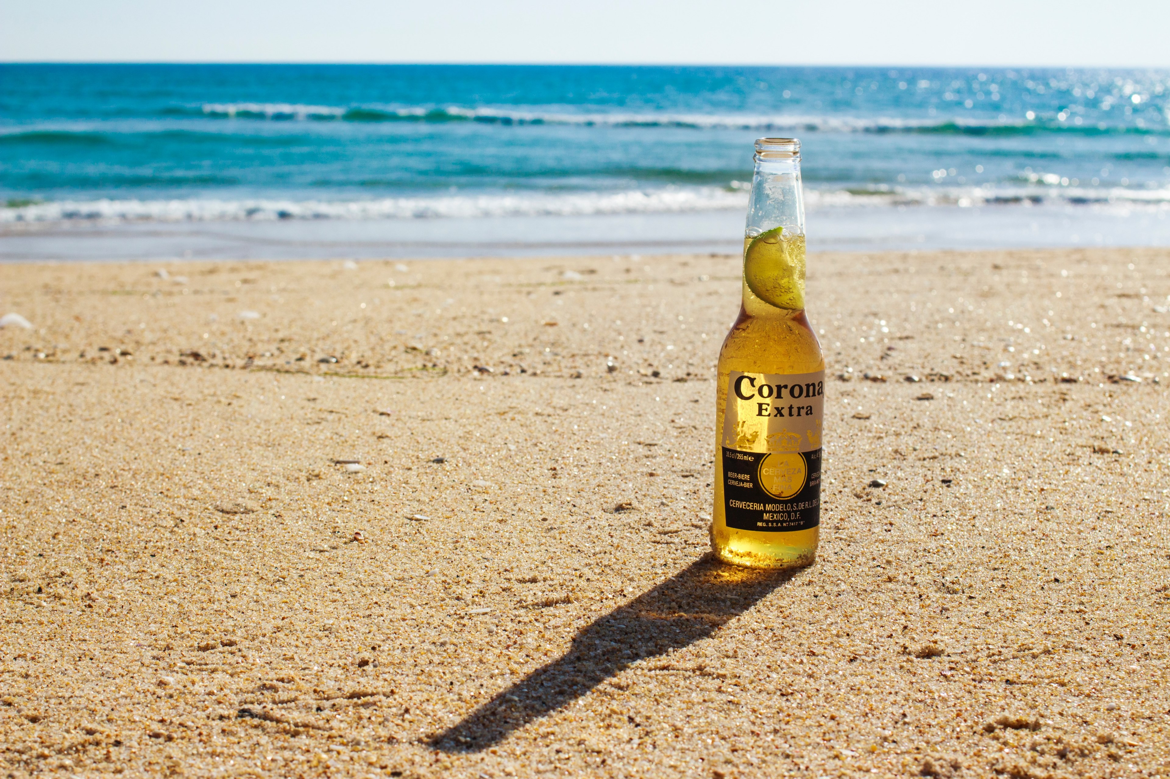 a bottle of beer with a lime slice on coarse sand by the sea, beer on the beach 4k, HD Wallpaper