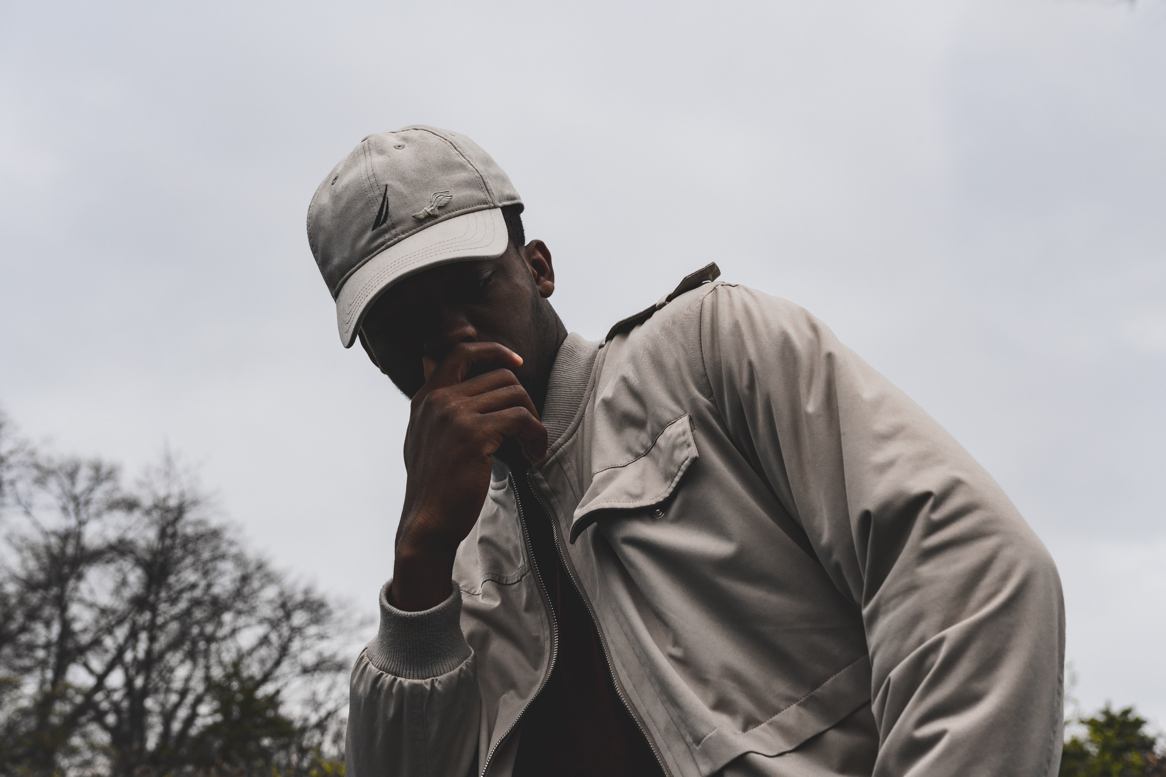 a man in a gray baseball cap and jacket leans against his hand outdoors, man leaning against his hand 4k, HD Wallpaper