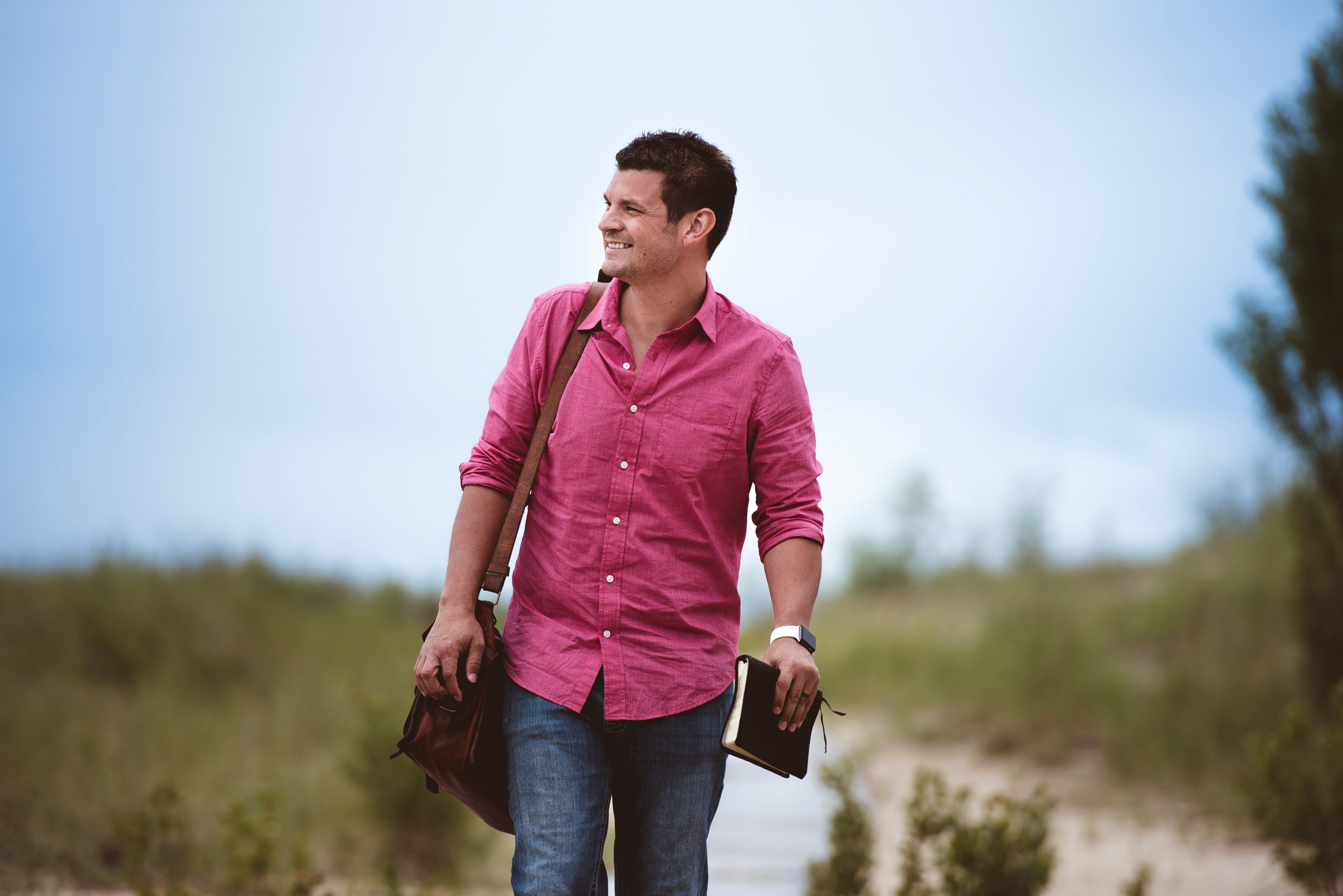 a man in a pink shirt with a leather bag and a book walking on a dirt path, man holding leather bound book 4k, HD Wallpaper