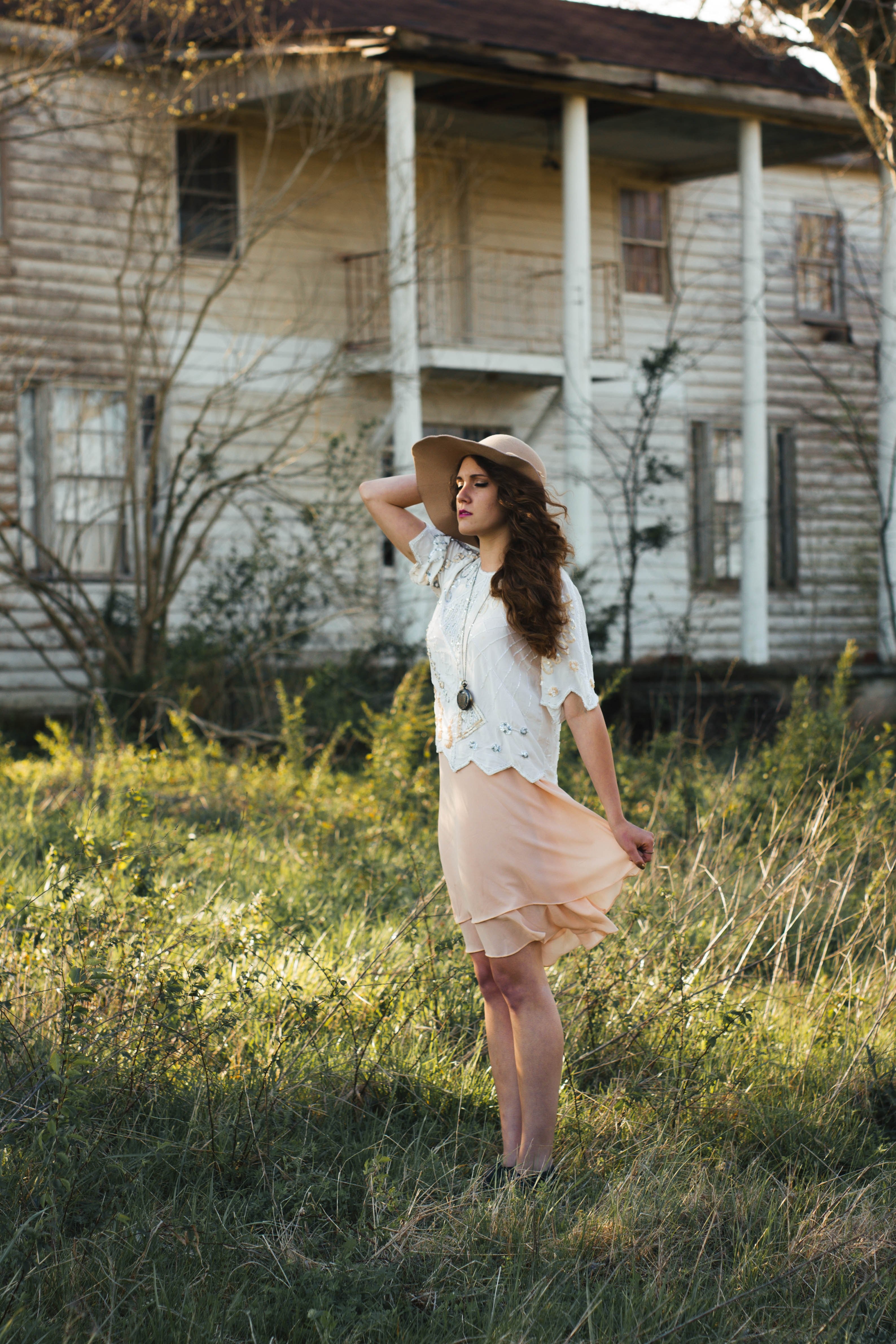 woman in a peachy skirt with a white blouse standing in front of a decaying white house, feeling the wind 4k, Phone HD Wallpaper