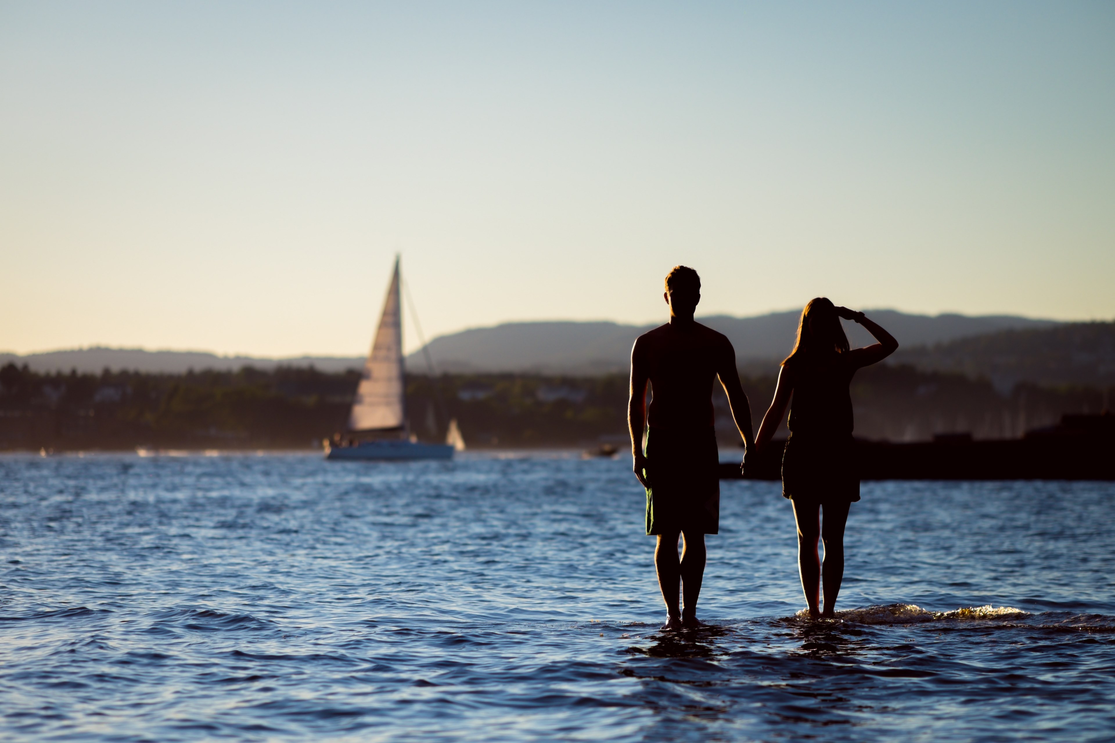 man and woman standing in the bay watching a sailboat pass by, in the bay 4k, HD Wallpaper