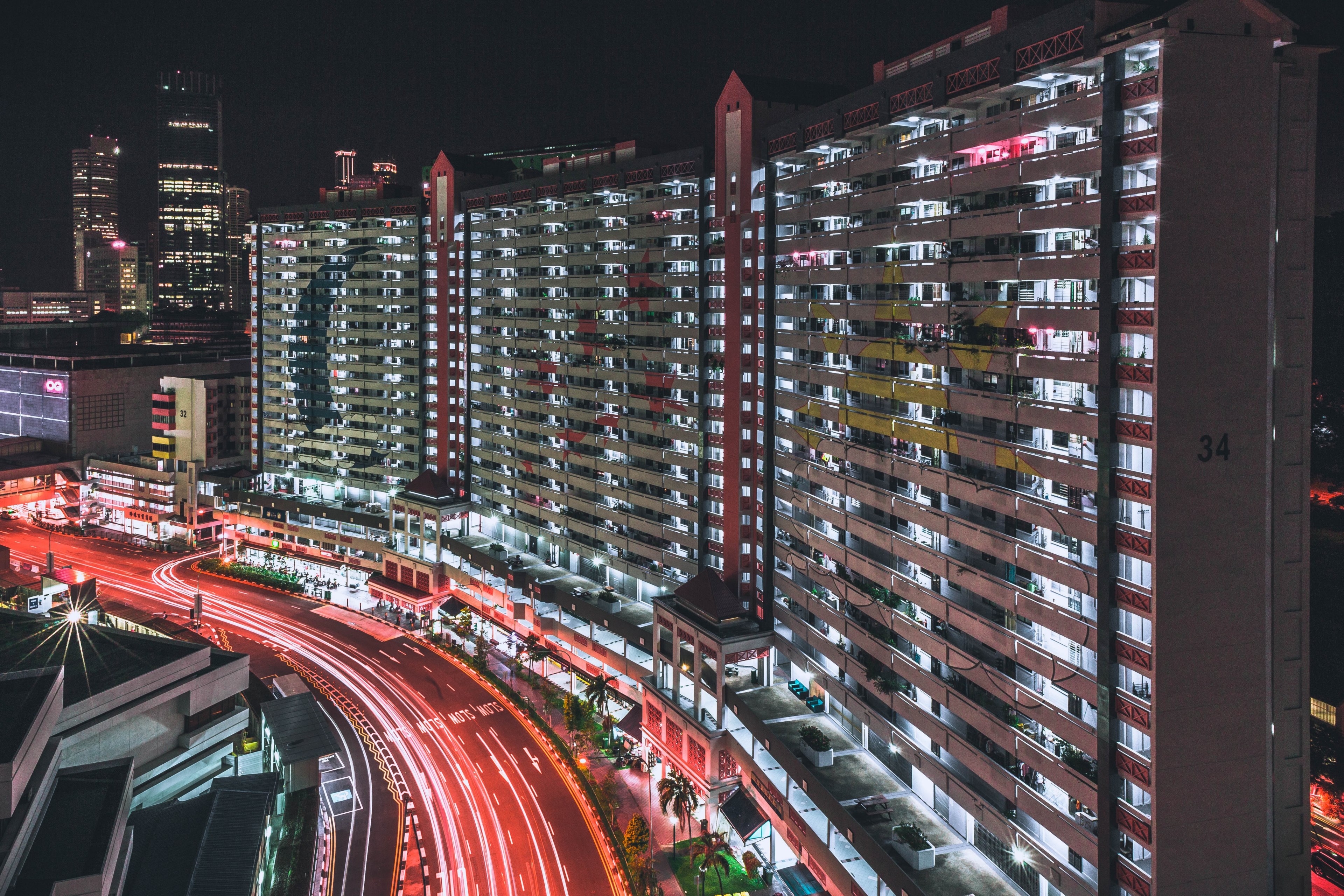 a wide thin apartment complex broken up into three sections with commercial properties at the bottom surrounded by trailing car lights and skyscrapers, city building 4k, HD Wallpaper