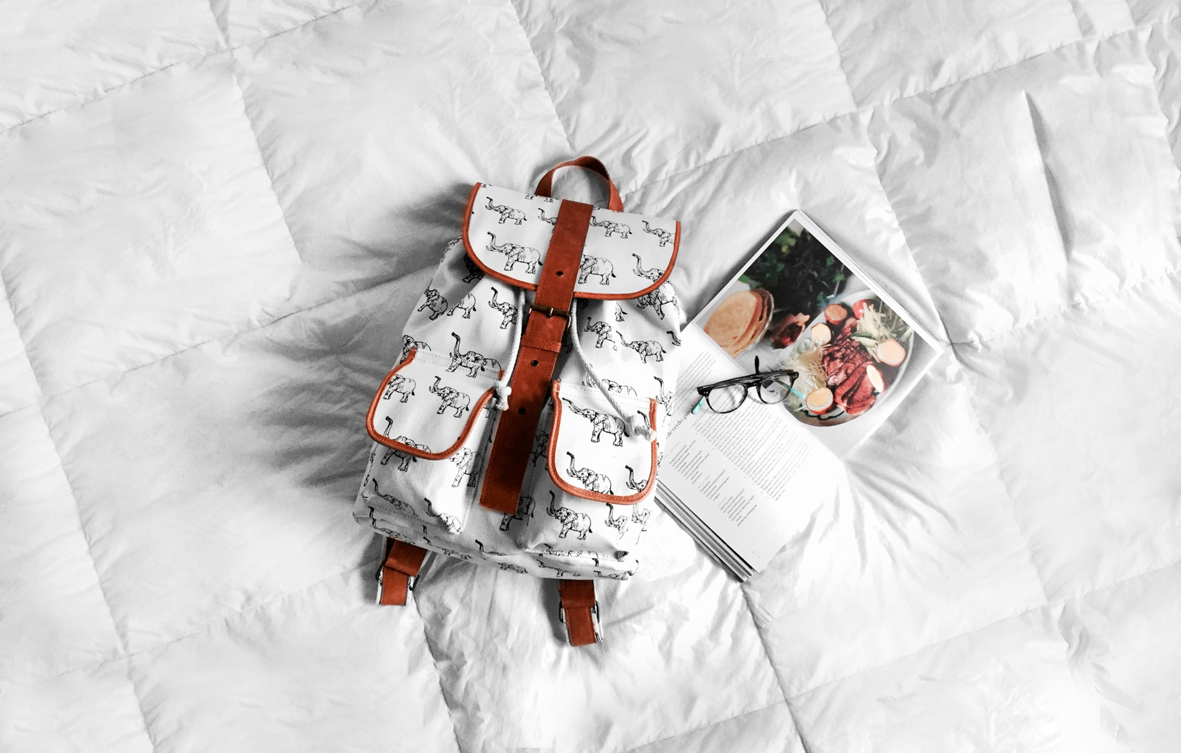 a white backpack on a bed mattress next to a cookbook and a pair of glasses, backpack and cookbook on a bed 4k, HD Wallpaper