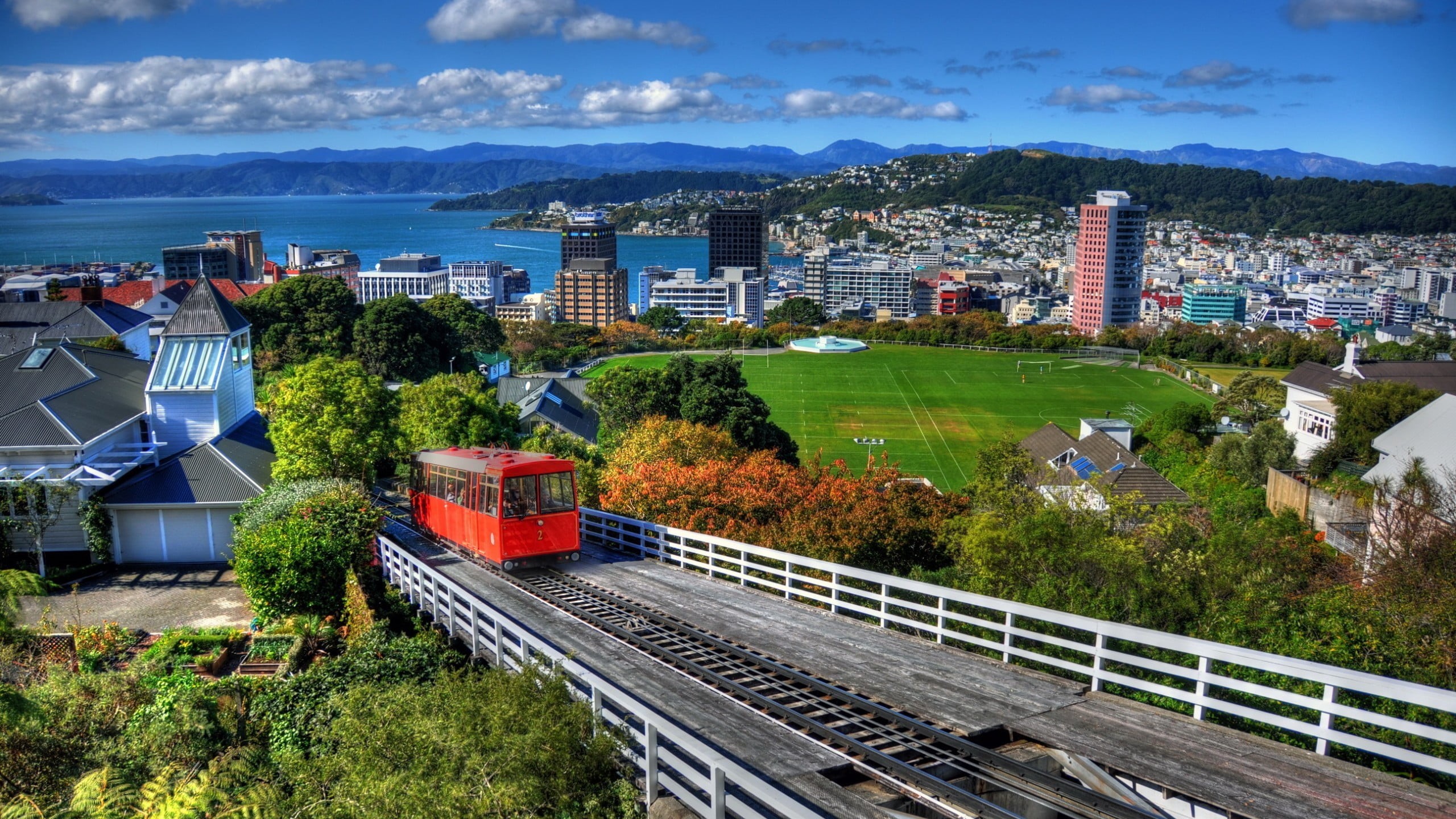 architecture, public transportation, mode of transportation, nature, trees, rail, hills, built structure, 2K, city, cityscape, Soccer Field, office building exterior, HD Wallpaper