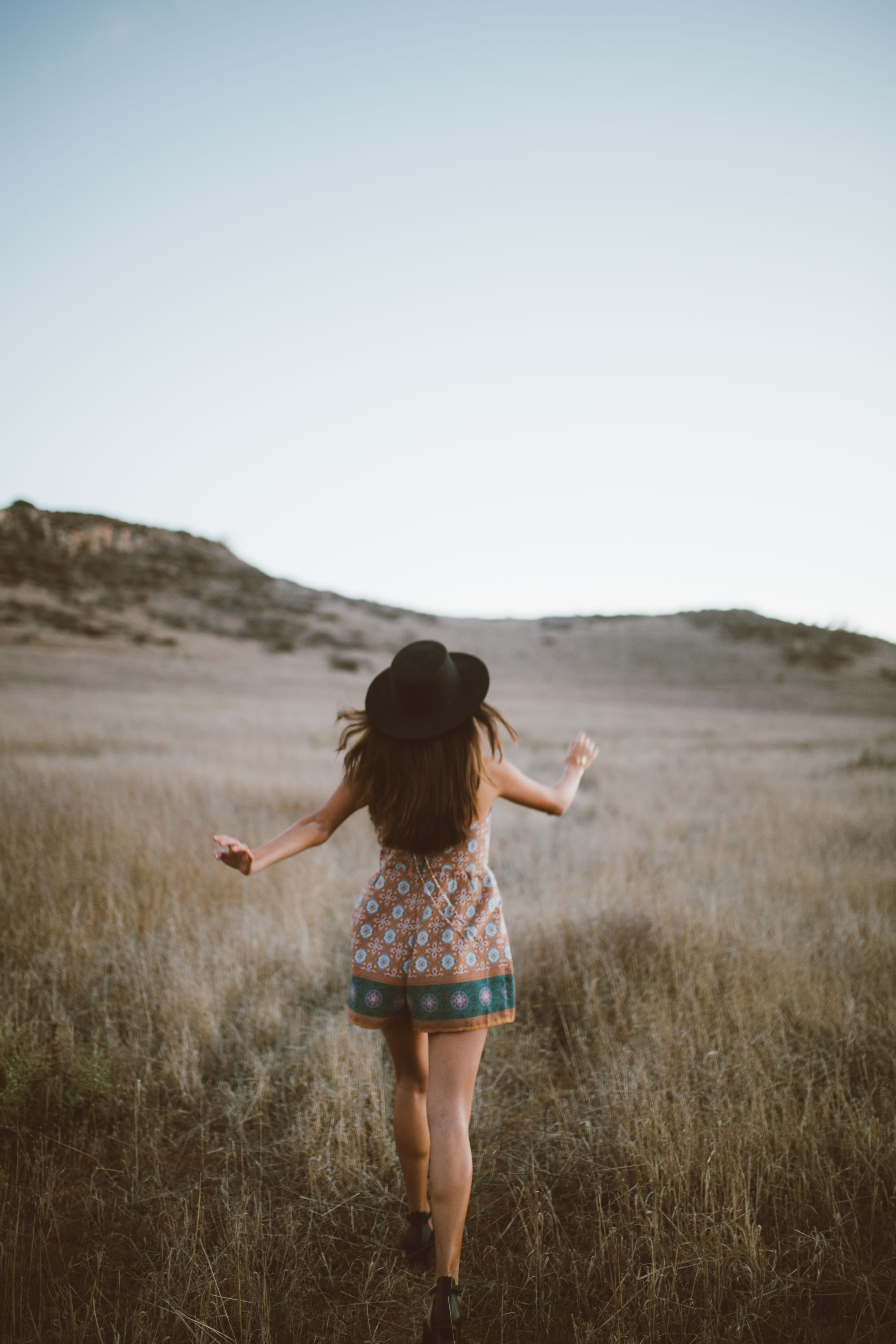 romper, grass, women, outdoors, leisure activity, brown, beauty In Nature, field, woman, green, one woman only, daytime, arms Outstretched, black hat, adult, Phone HD Wallpaper