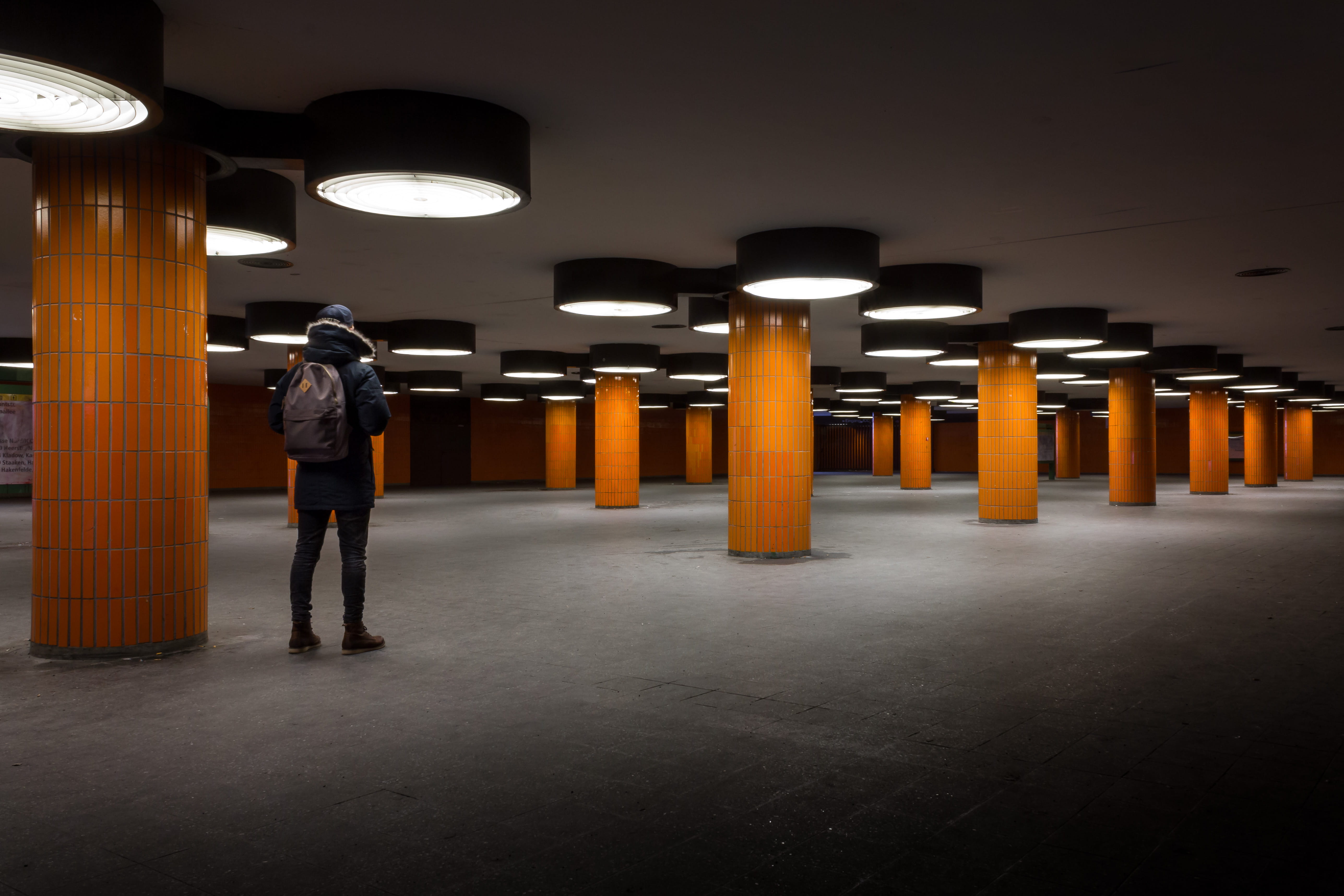 person, man in black, post, parking, standing, leisure activity, backpack, underground, electric lamp, people, adult, lot, wearing, full length, light, HD Wallpaper