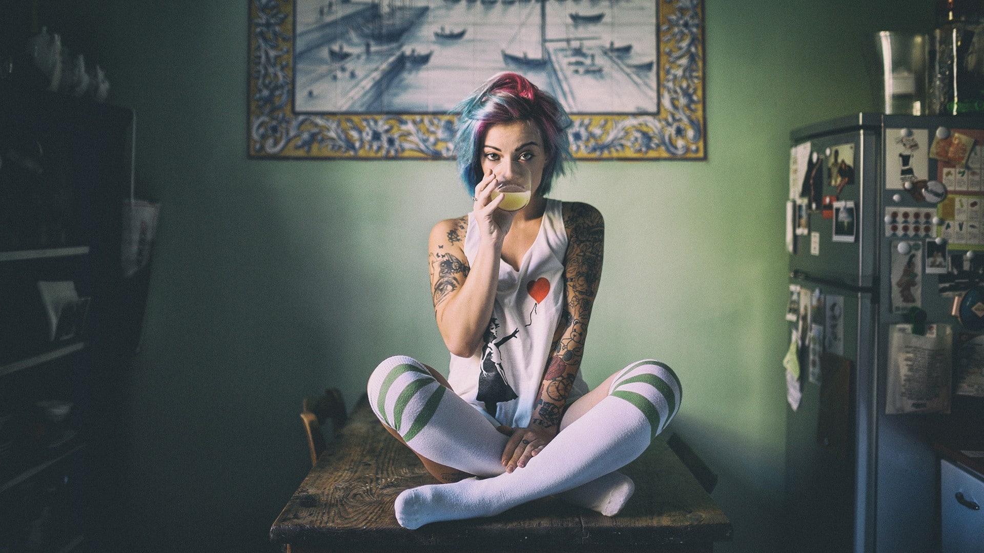 model, looking at viewer, 1080P, legs crossed, sitting, knee-highs, dyed hair, table, kitchen, tattoo, women, drinking glass, T-shirt, striped leggings, HD Wallpaper