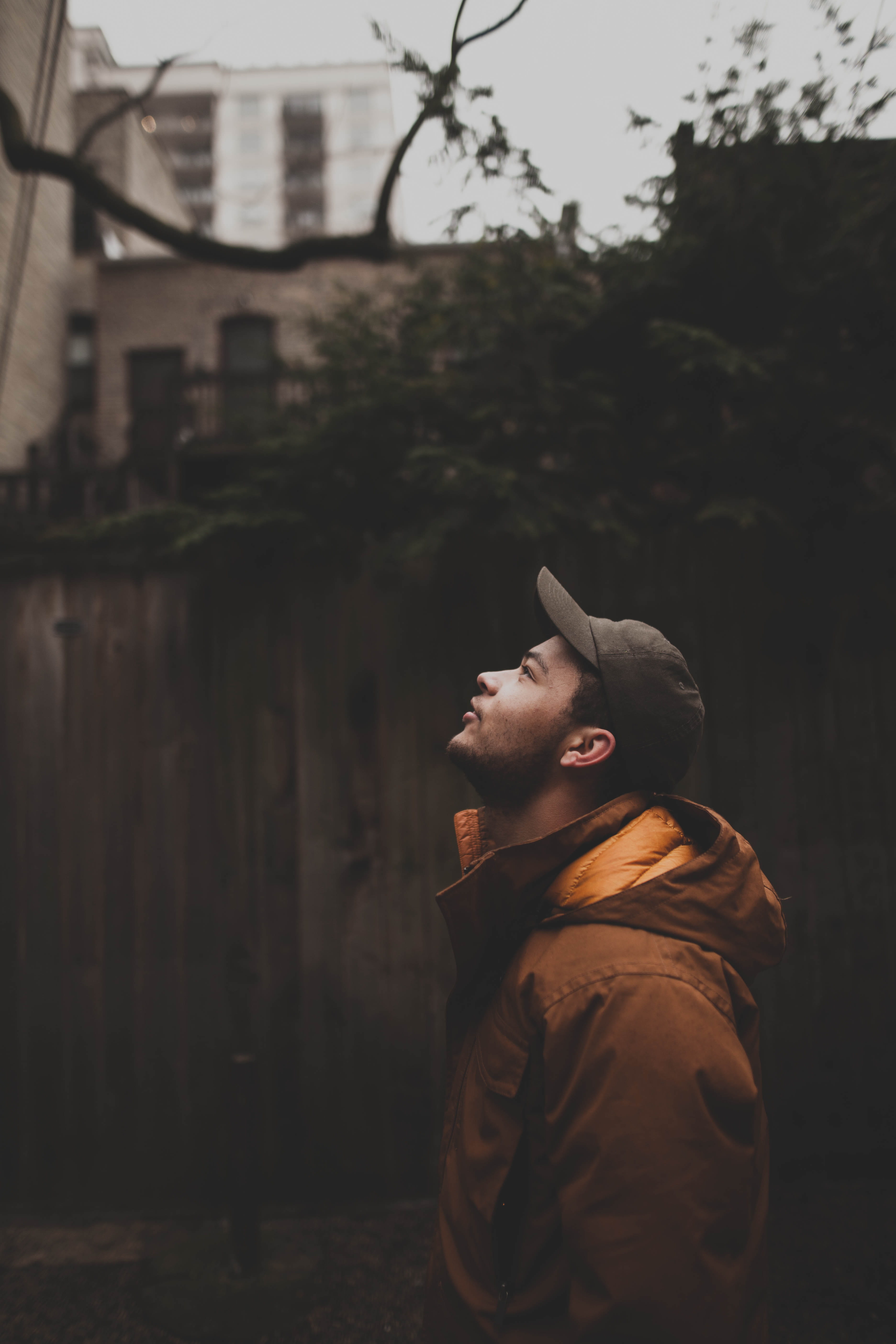 cap, looking, outdoors, staring, contemplation, warm clothing, tree, focus on foreground, lifestyles, male, brown, architecture, leisure activity, gray, Phone HD Wallpaper
