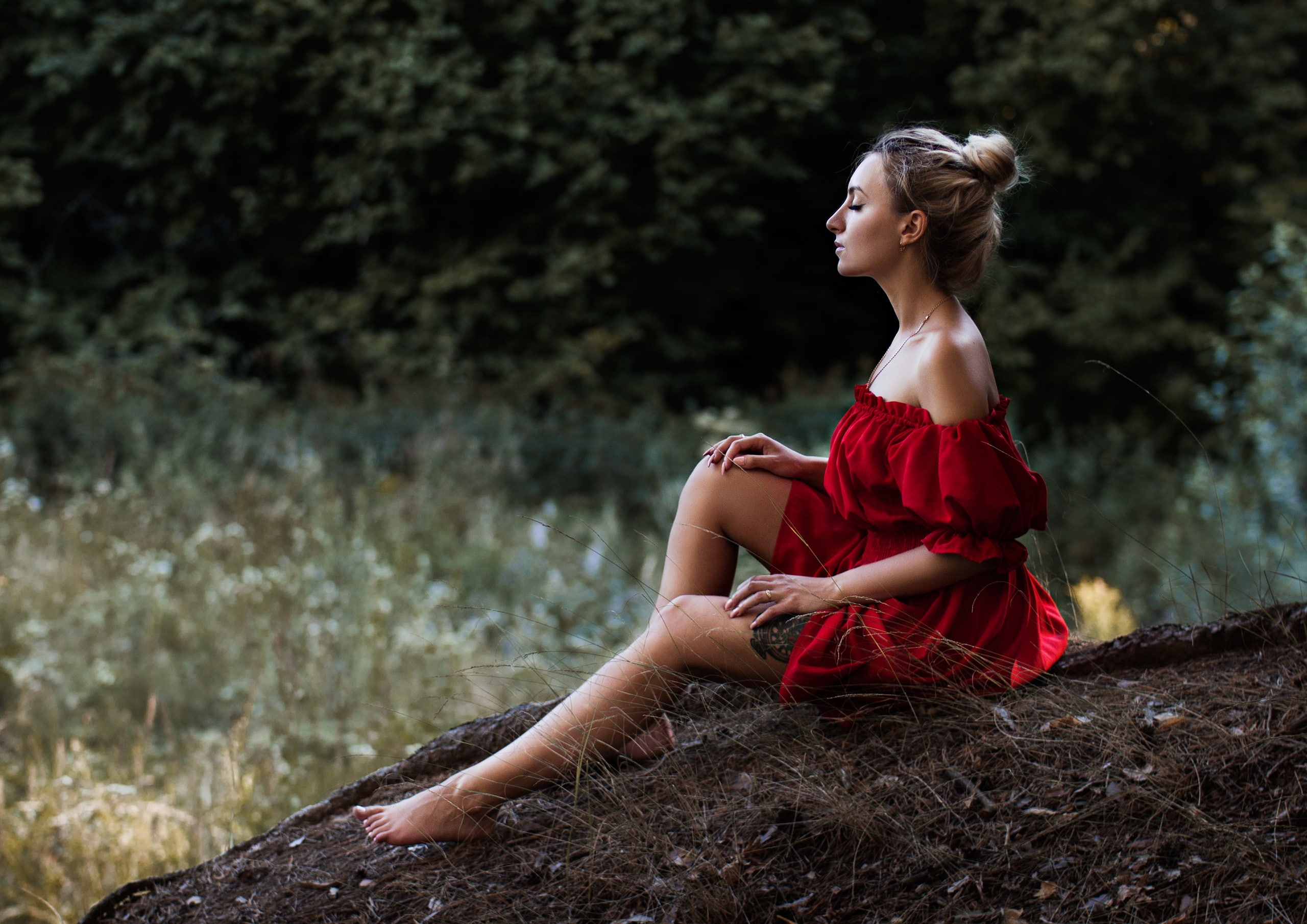 blonde, forest, model, women, profile, women outdoors, tattoo, hairbun, red dress, 2K, legs, dress, barefoot, bare shoulders, closed eyes, sitting, HD Wallpaper