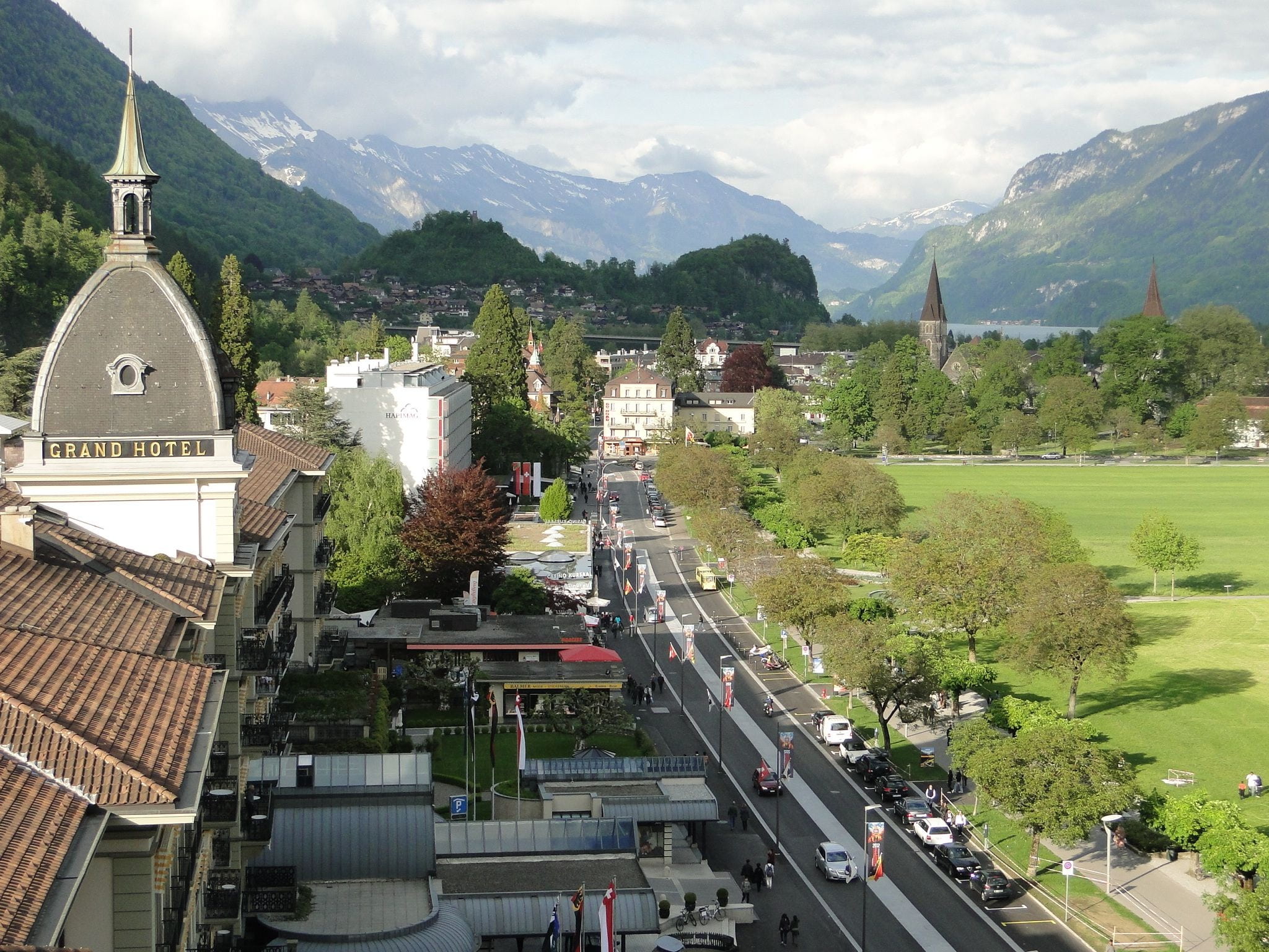 city, interlaken, street, incidental people, mountains, road, plant, 1080P, car, switzerland, built structure, sky, mountain range, landscape, europe, HD Wallpaper