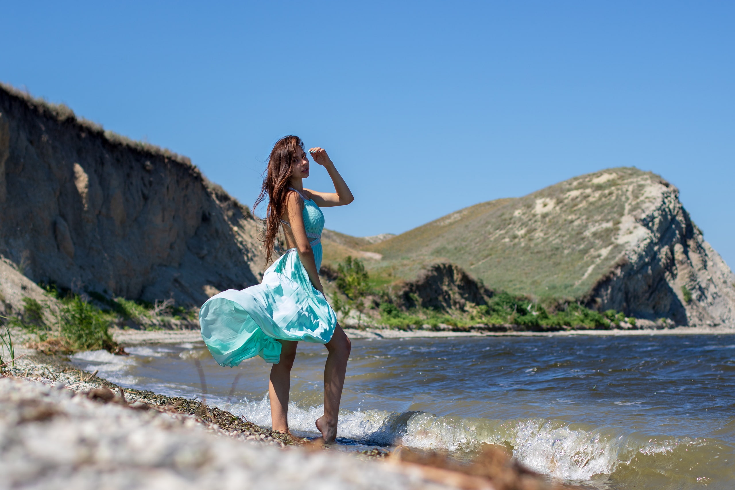 bokeh, blue dress, depth of field, looking at viewer, brunette, windy, shore, sky, long hair, rocks, painted nails, clear sky, photography, women outdoors, HD Wallpaper
