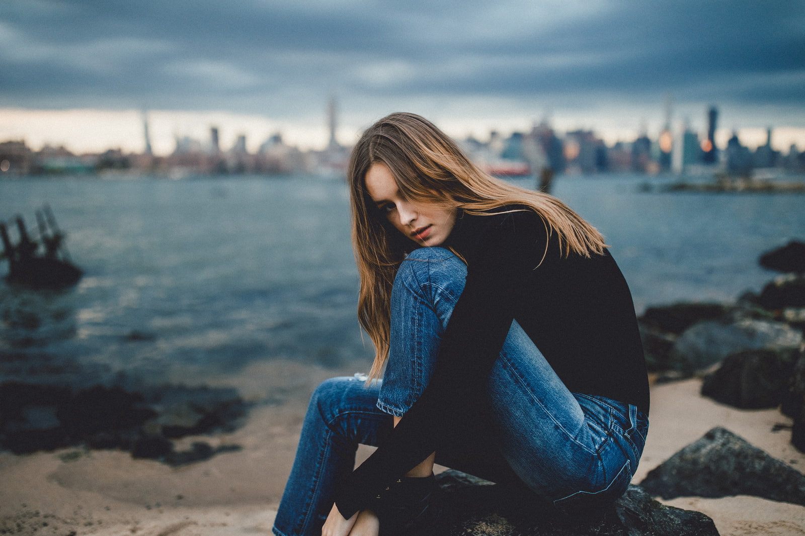 rocks, sea, turtlenecks, women outdoors, model, looking at viewer, jeans, brunette, Caitlin Nusche, 720P, sitting, SamAlive, depth of field, hair in face, HD Wallpaper