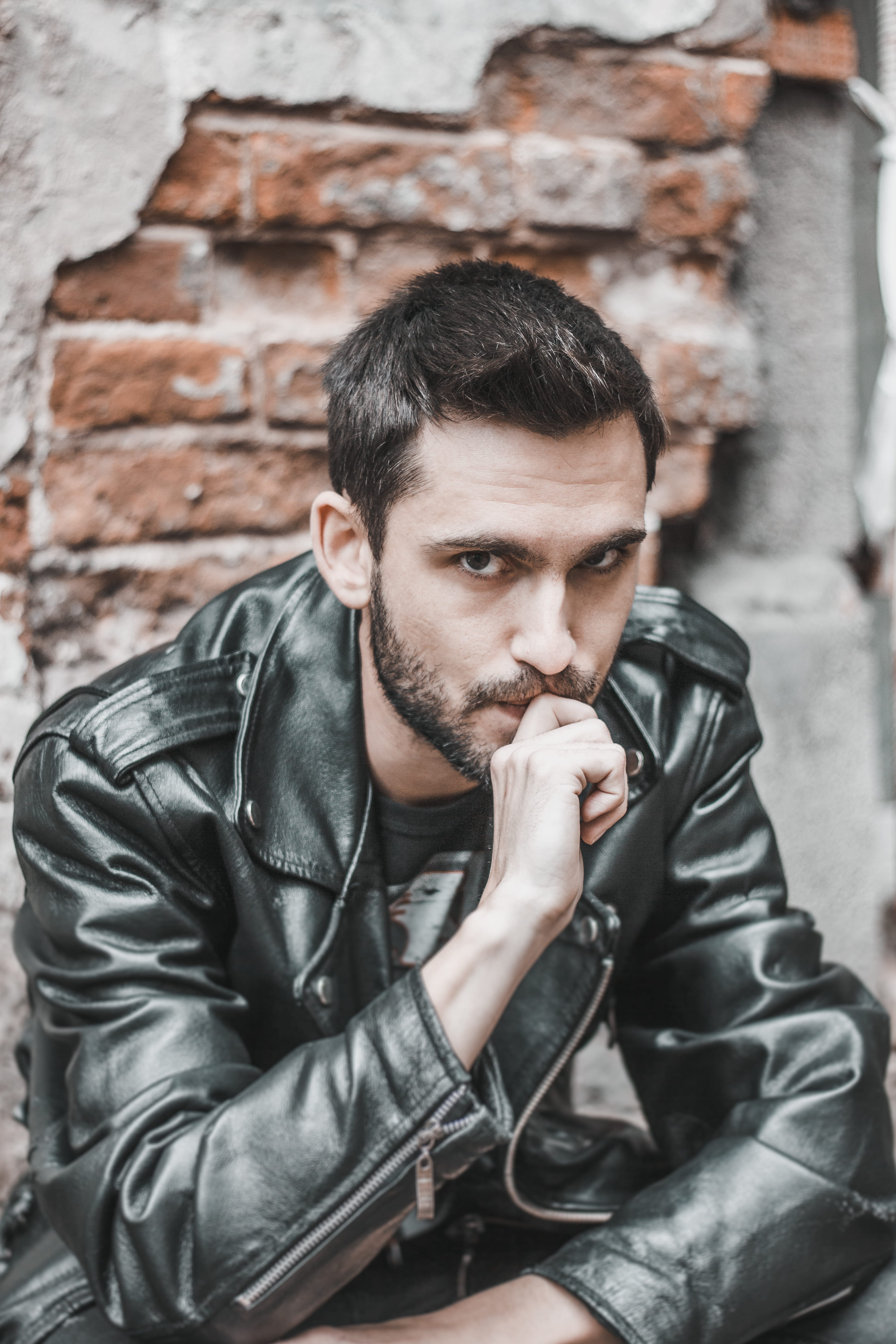 photo, portrait, front view, handsome, facial hair, posing, finger, sitting, young men, young adult, clothing, jacket, brick, architecture, biting, lifestyles, Phone HD Wallpaper