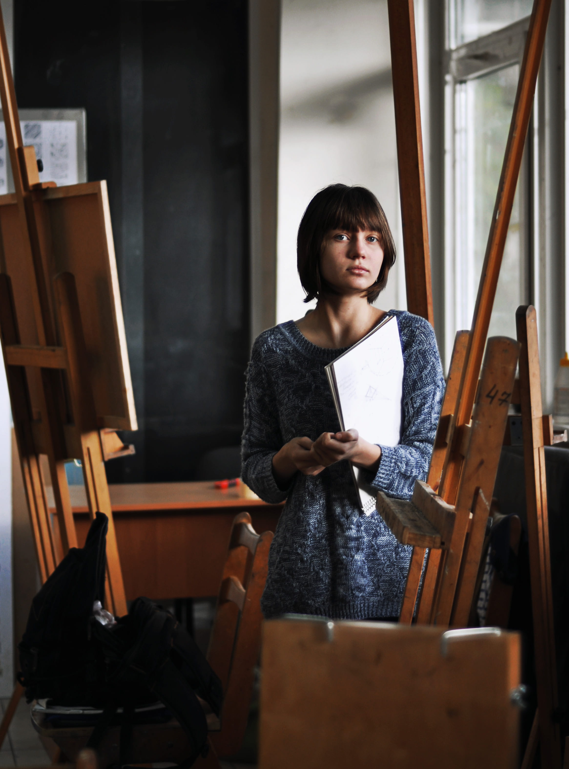 easel, casual clothing, papers, wood, 2K, style, chair, child, near, seat, indoors, holds, female, portrait, person, woman, holding, sketchbook, artist, Phone HD Wallpaper