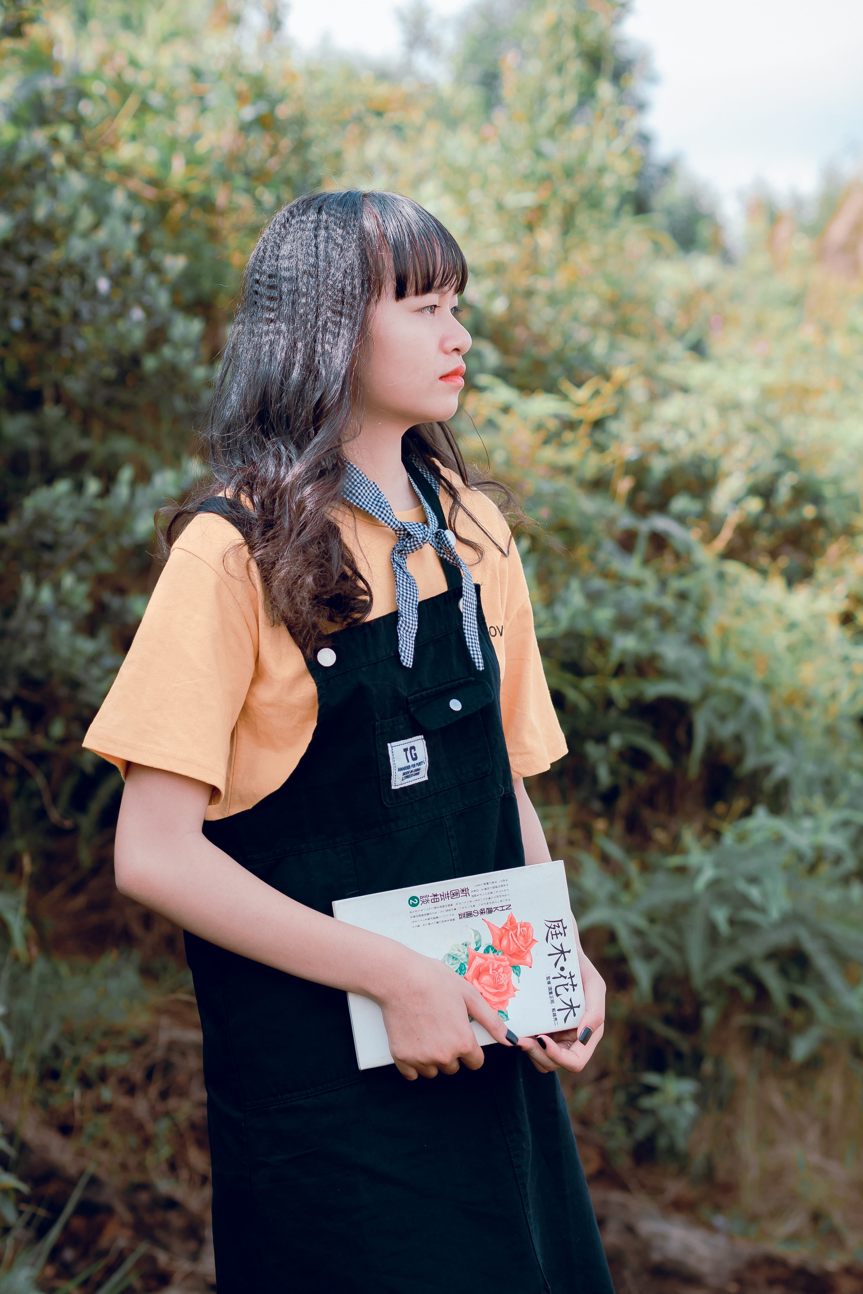 field, beautiful woman, day, three quarter length, standing, looking, orange, beauty, pretty, shirt, dungaree, black, real people, looking away, holding, Phone HD Wallpaper