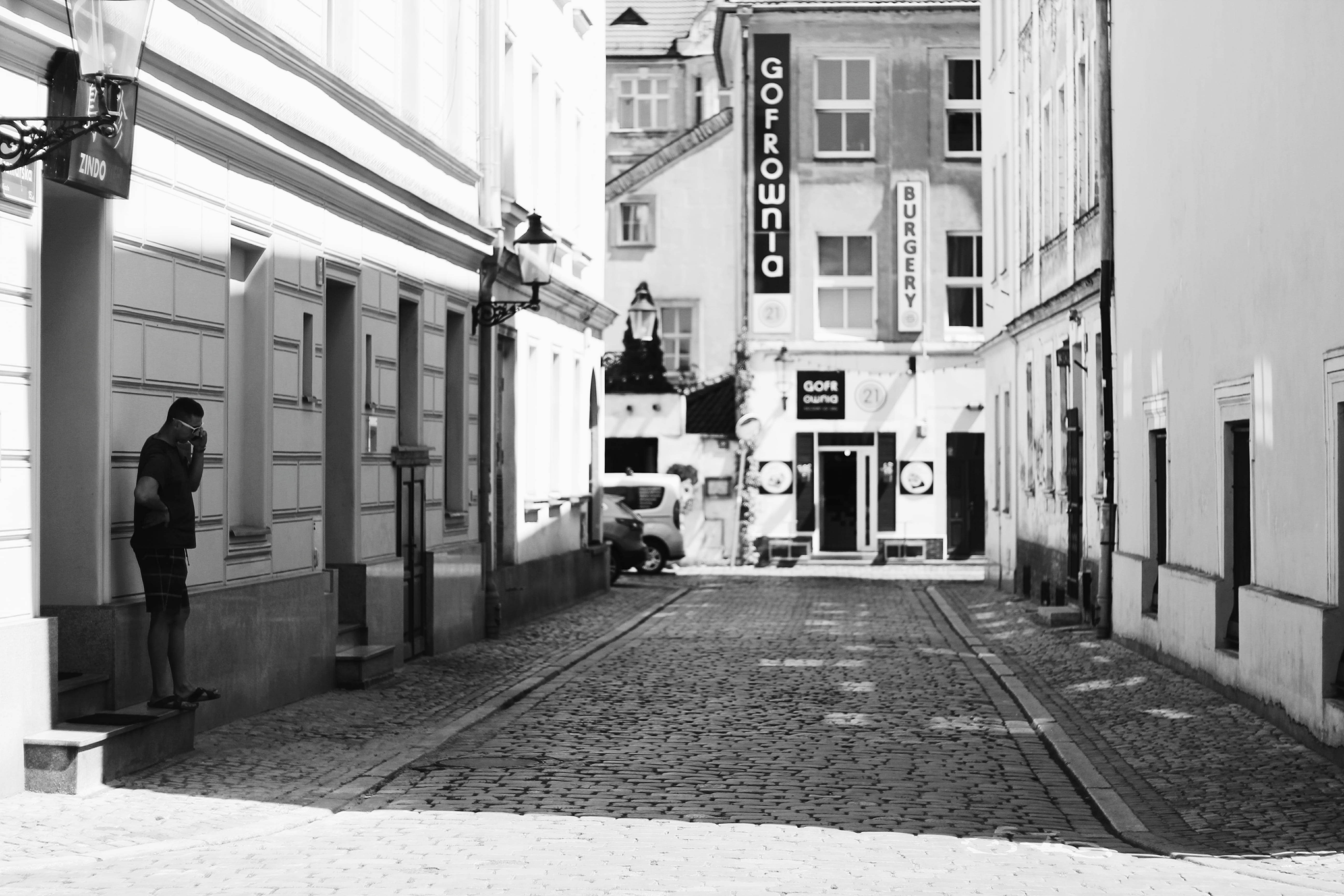 outdoors, real people, pavement, building exterior, building, monochrome, residential district, photography, man, lamppost, vehicle, direction, buildings, HD Wallpaper
