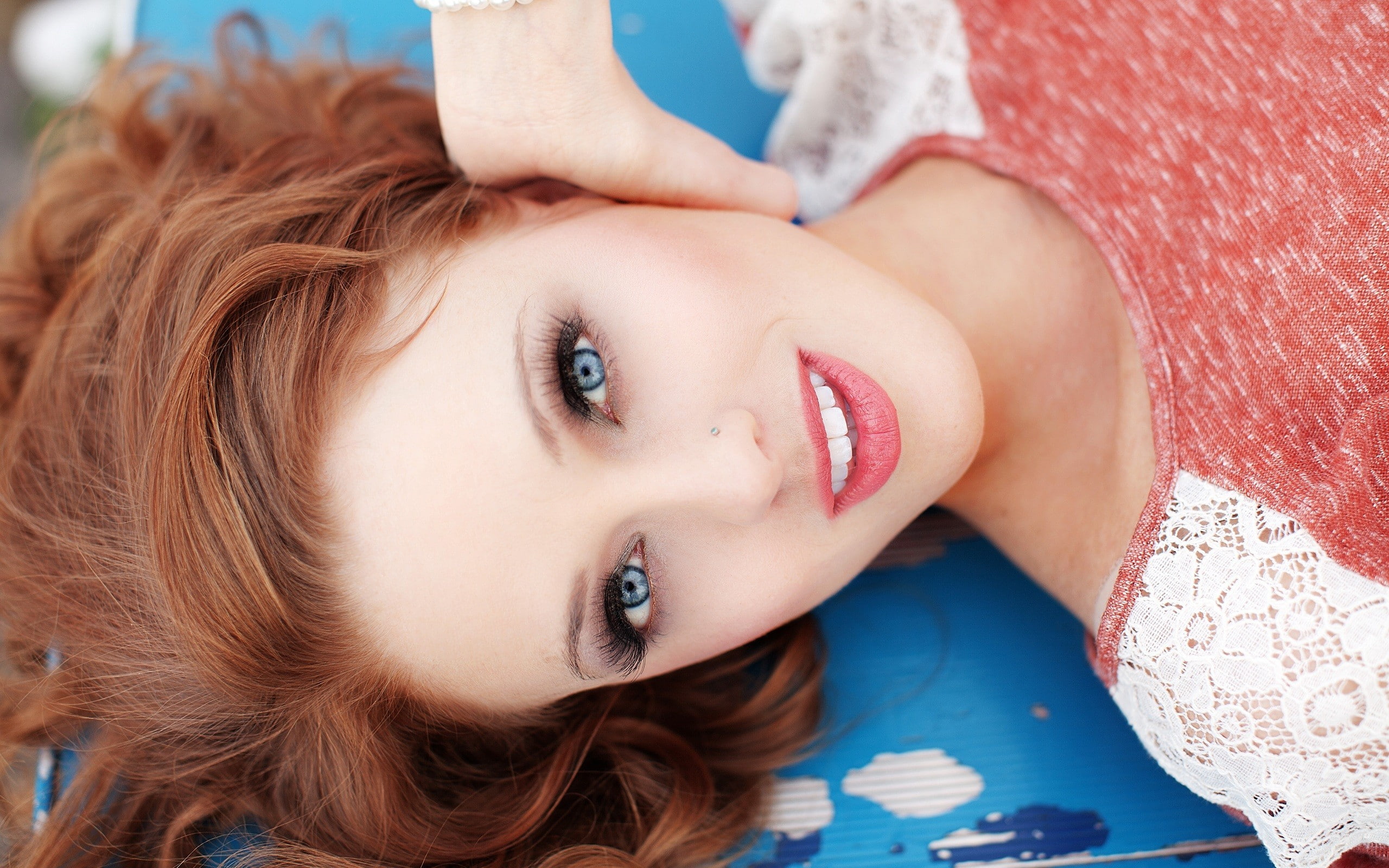 model, looking at viewer, lying on back, blue eyes, open mouth, piercing, pierced nose, smiling, redhead, women, face, long hair, 2K, women outdoors, makeup, HD Wallpaper