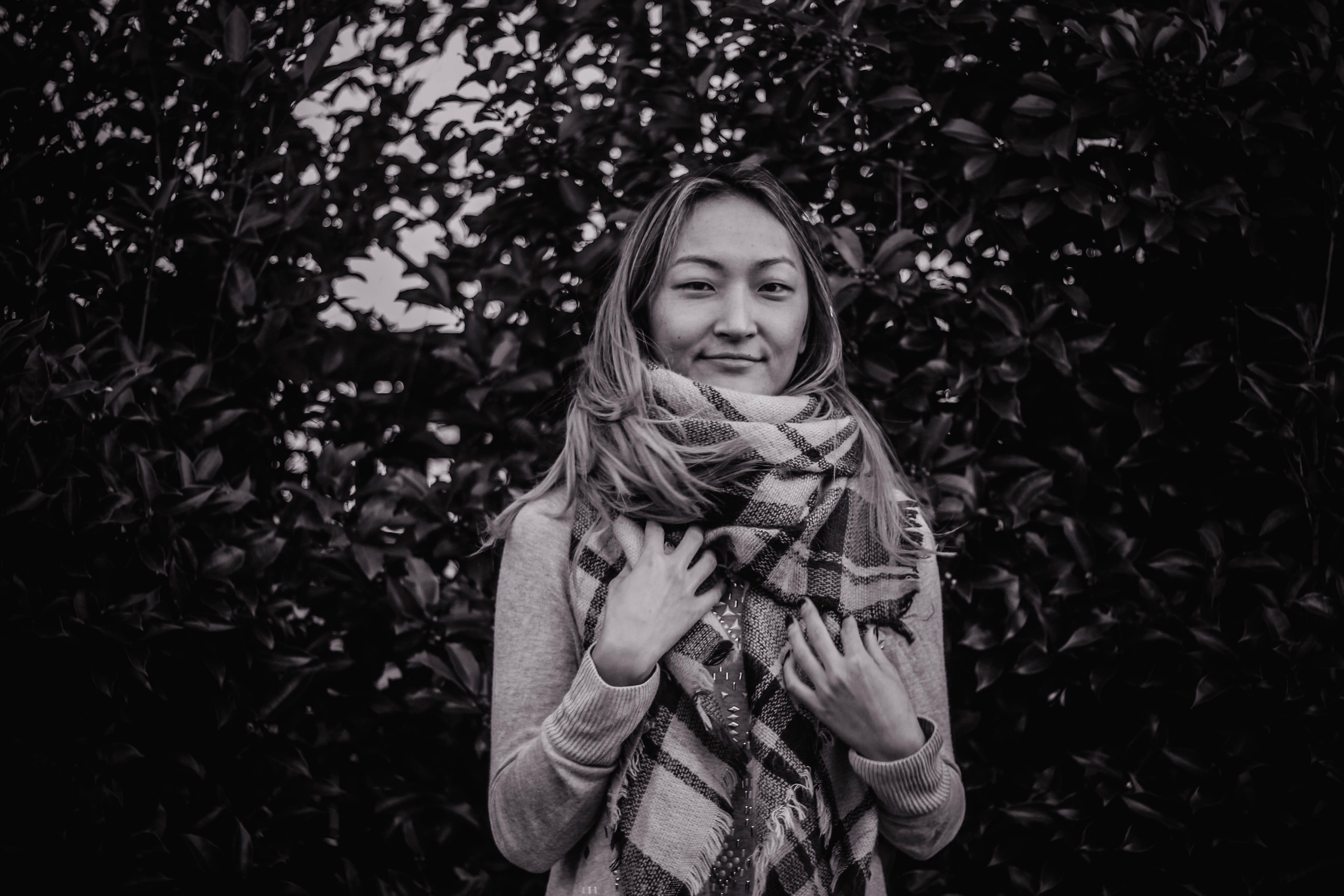 grayscale, woman, childhood, 5K, person, wearing, apparel, hairstyle, warm clothing, smiling, girls, green bush, bush, leaf, portrait, face, leisure activity, HD Wallpaper