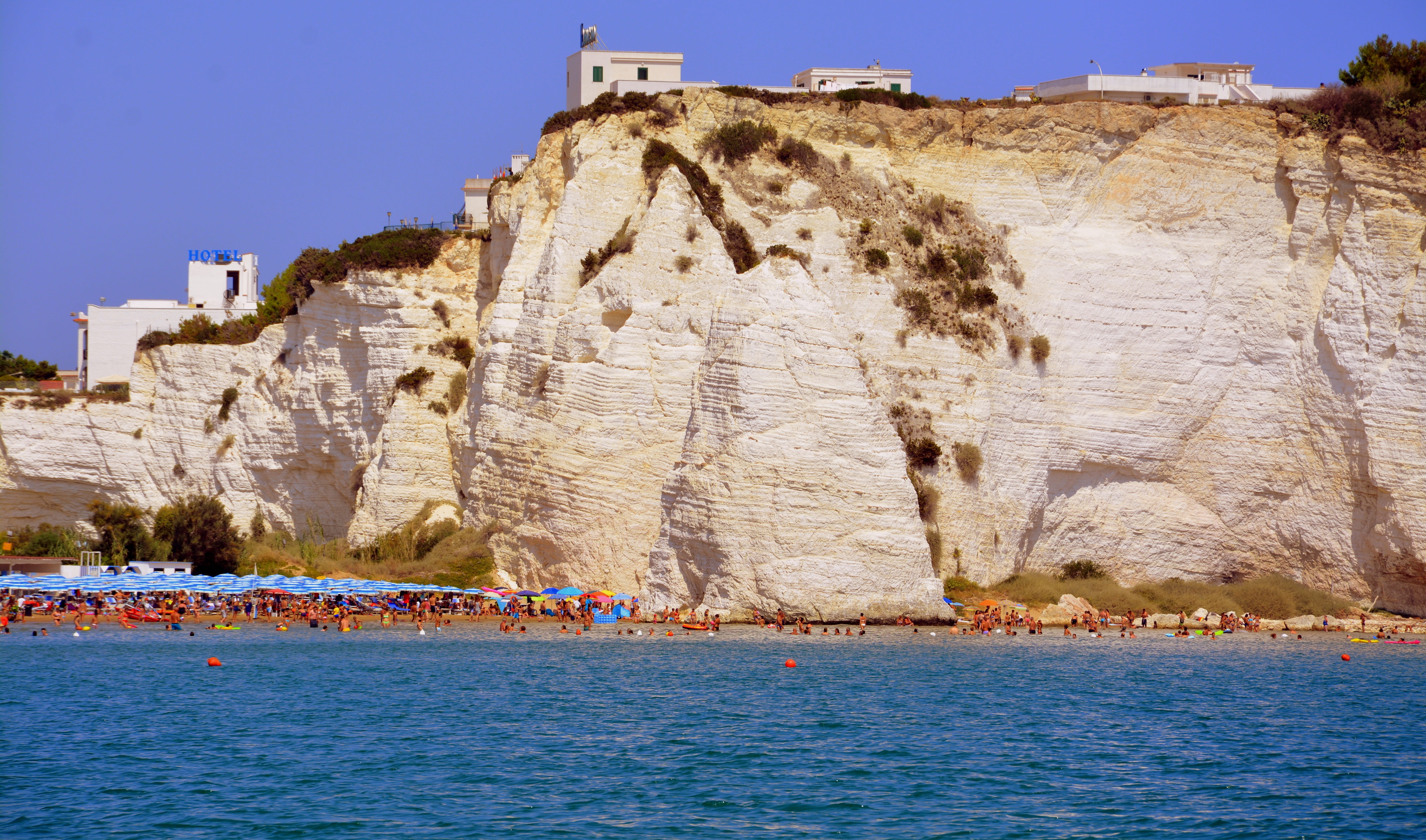 water, bathers, rock - object, nature, sea, umbrellas, cliff, houses, pizzomunno, beach, travel, 5K, eroded, day, blue, puglia, solid, outdoors, land, HD Wallpaper