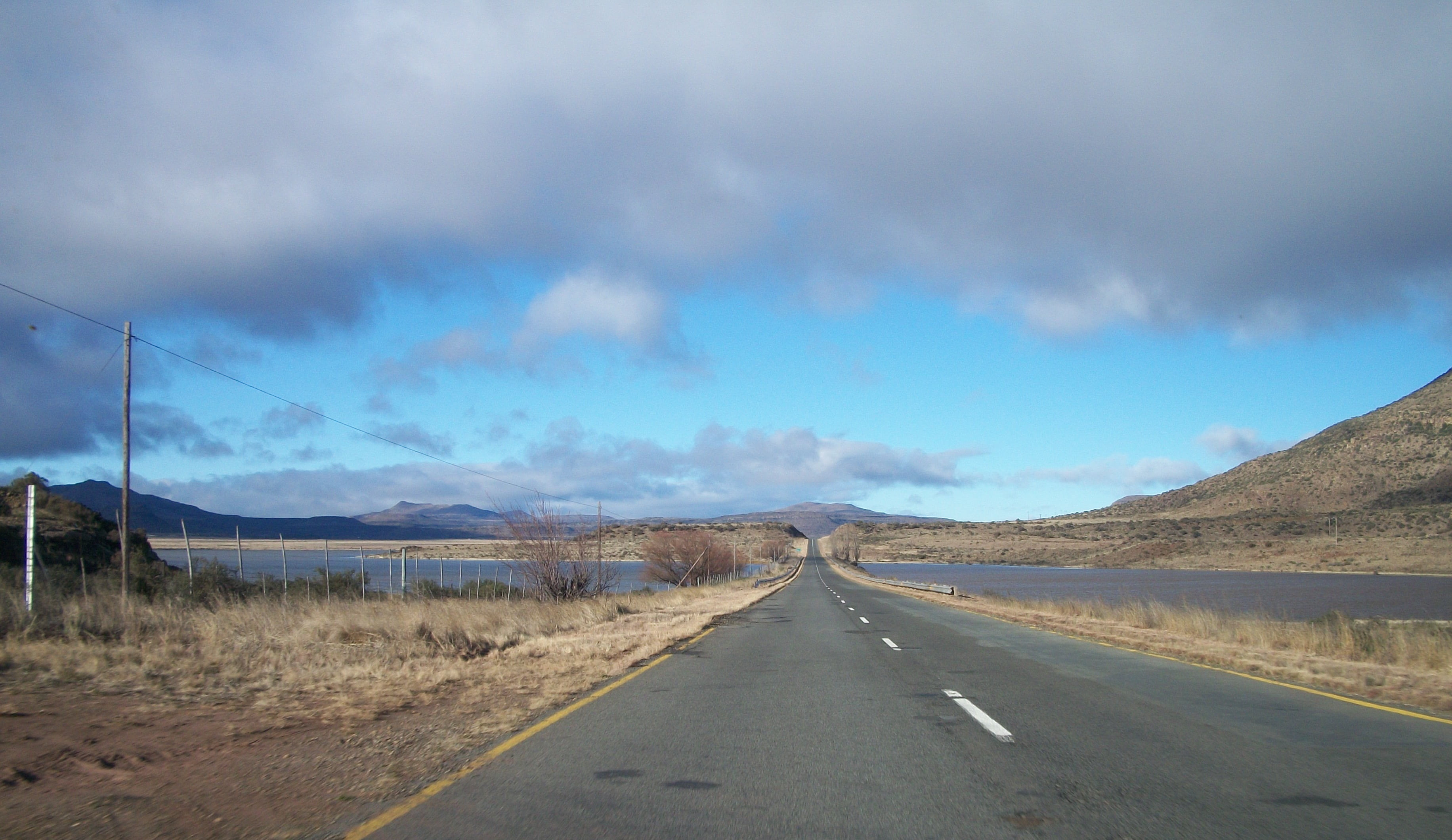 symbol, environment, clouds, no people, worn, travel, the way forward, road, mountain range, cloud - sky, straight, tarmac, landscape, sign, potholes, vanishing point, HD Wallpaper