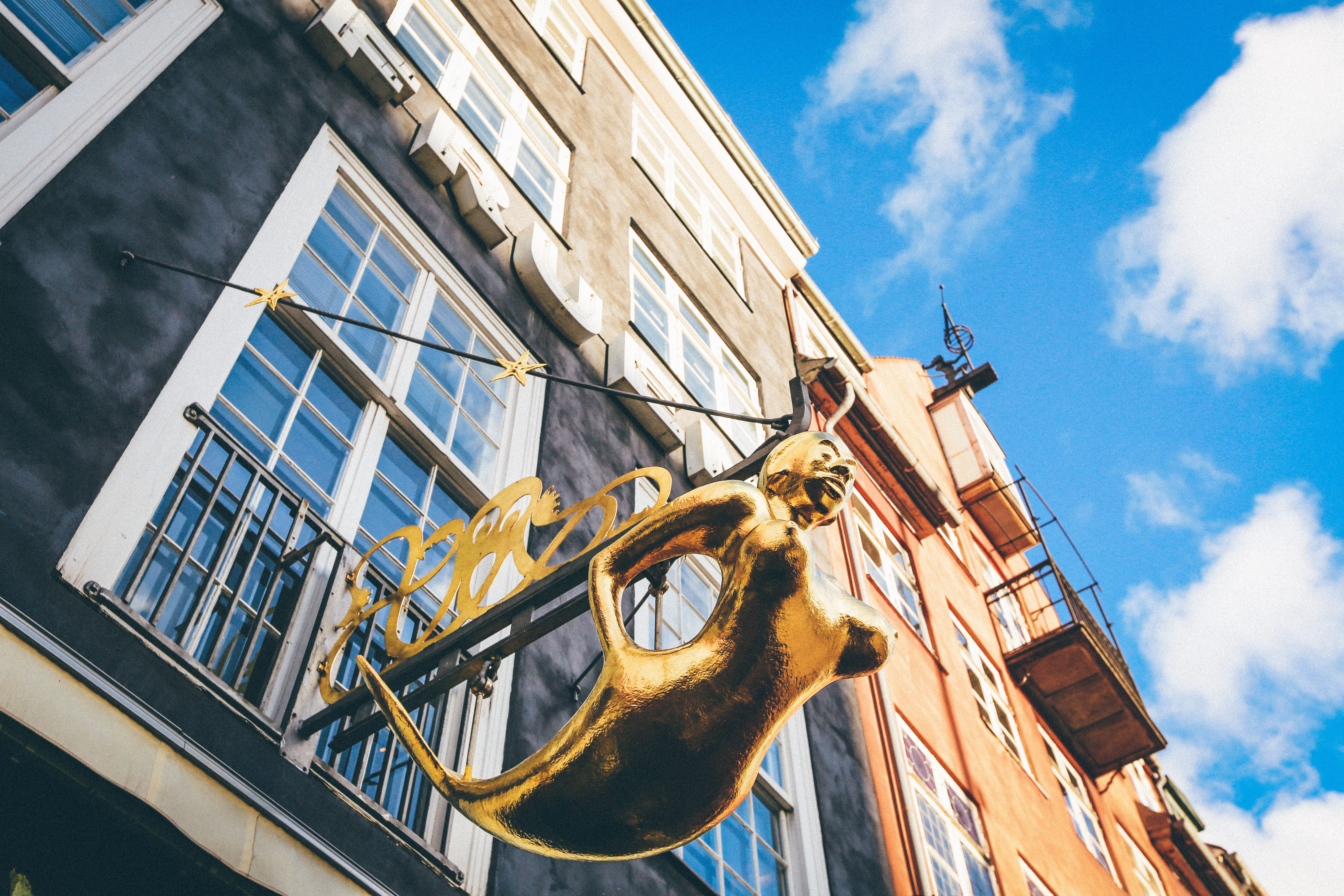 mermaid, low, outdoors, representation, building, 5K, gold, city, craft, photography, hanging, sunlight, low angle view, sculpture, architecture, building exterior, HD Wallpaper