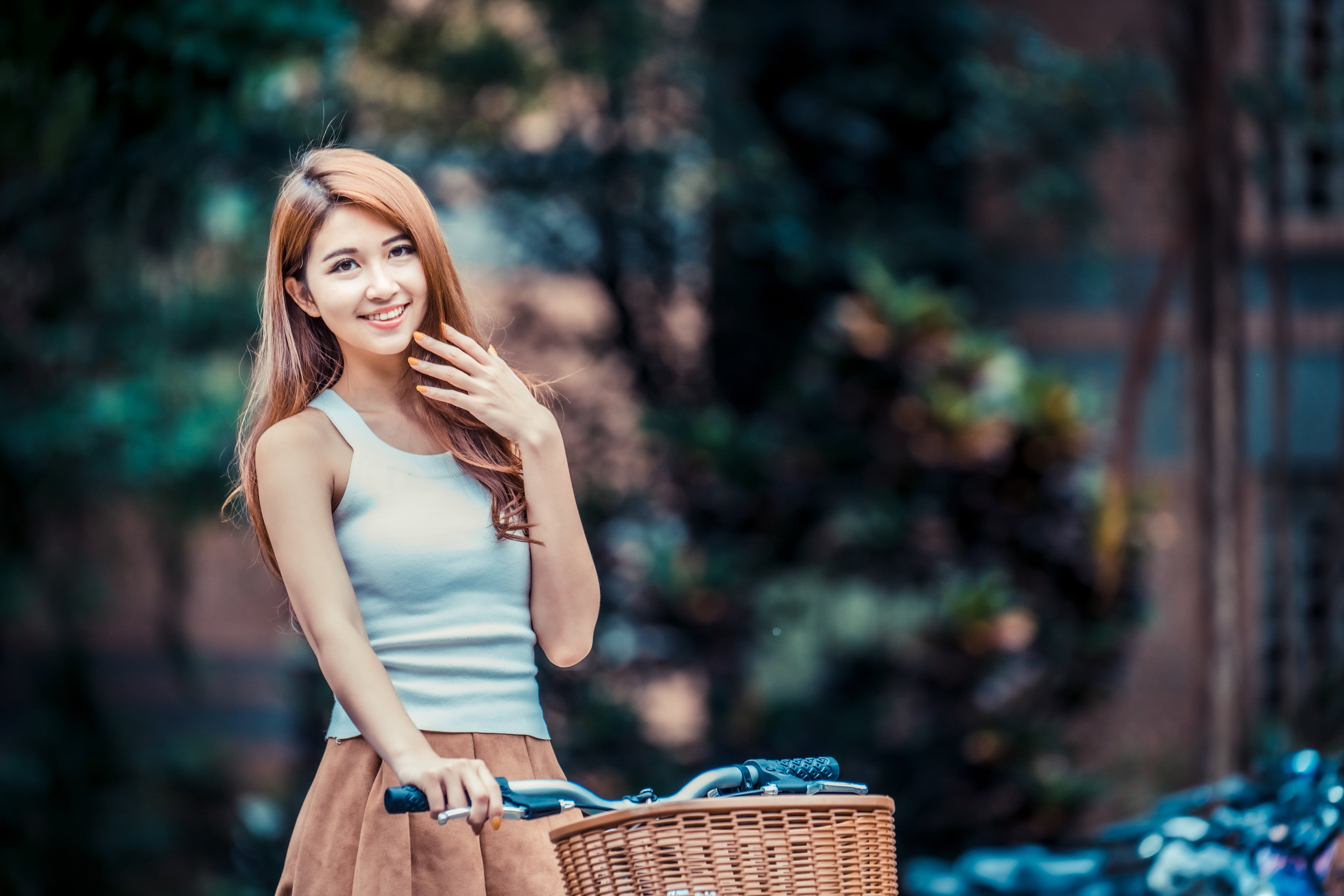 depth of field, long hair, smiling, Asian, skirt, brunette, bycicle, model, looking at viewer, trees, women, blue shirt, hand on face, 4K, HD Wallpaper