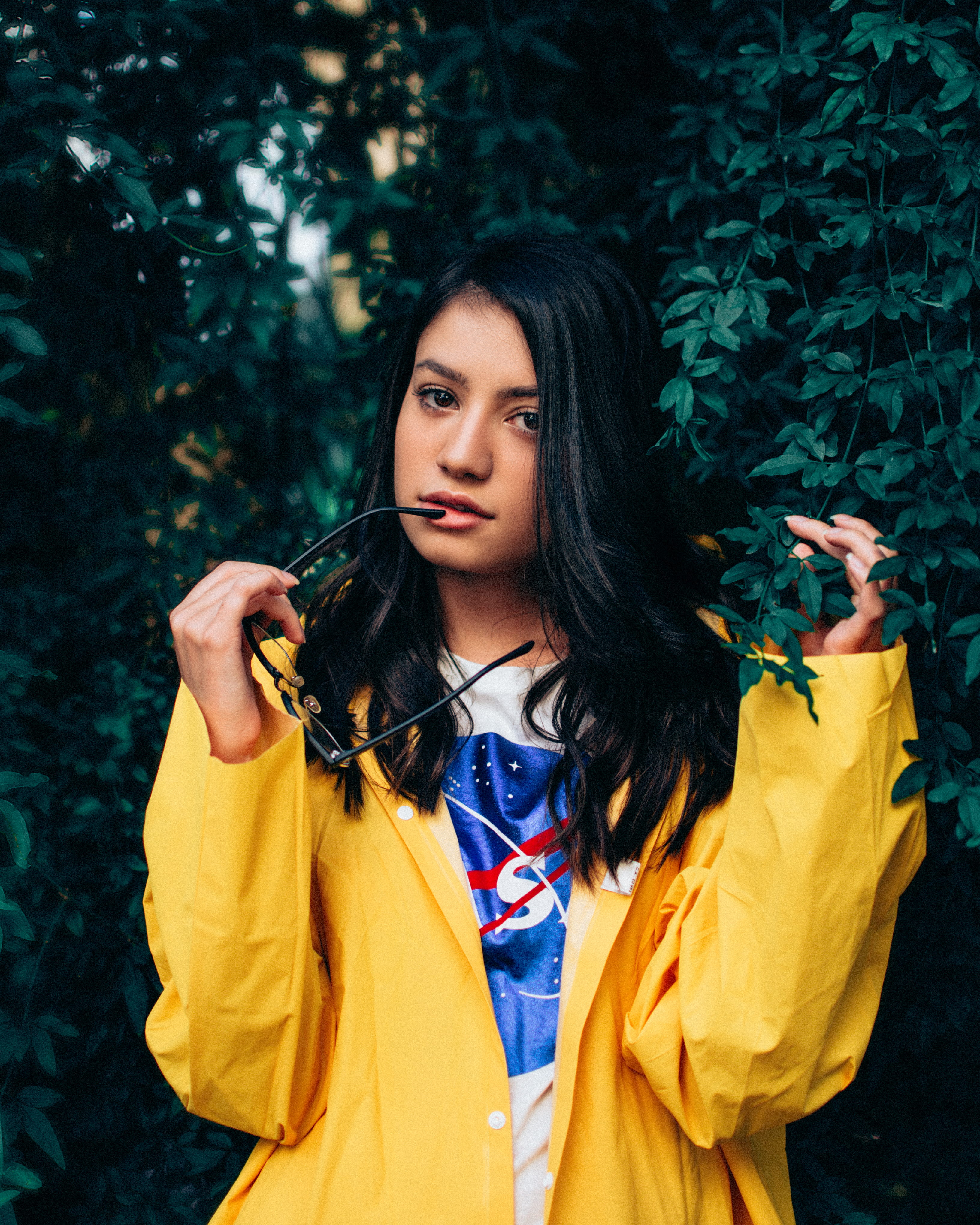 green, beside, eyeglasses, glasses, model, hair, black, standing, bush, lifestyles, warm clothing, women, long hair, beauty, front view, tree, yellow coat, Phone HD Wallpaper