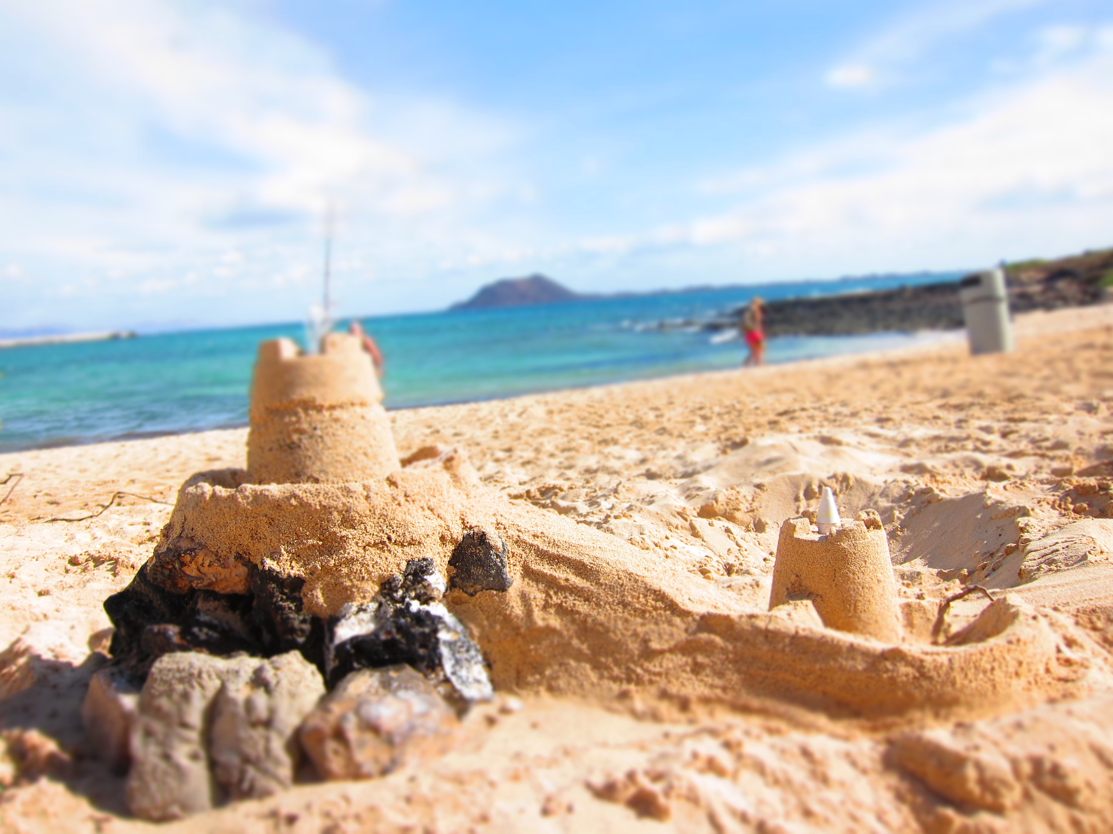 island, coastline, sand, sunlight, horizon, sand sculpture, sea, 2K, focus on foreground, sky, day, incidental people, water, land, sandcastle, horizon over water, HD Wallpaper