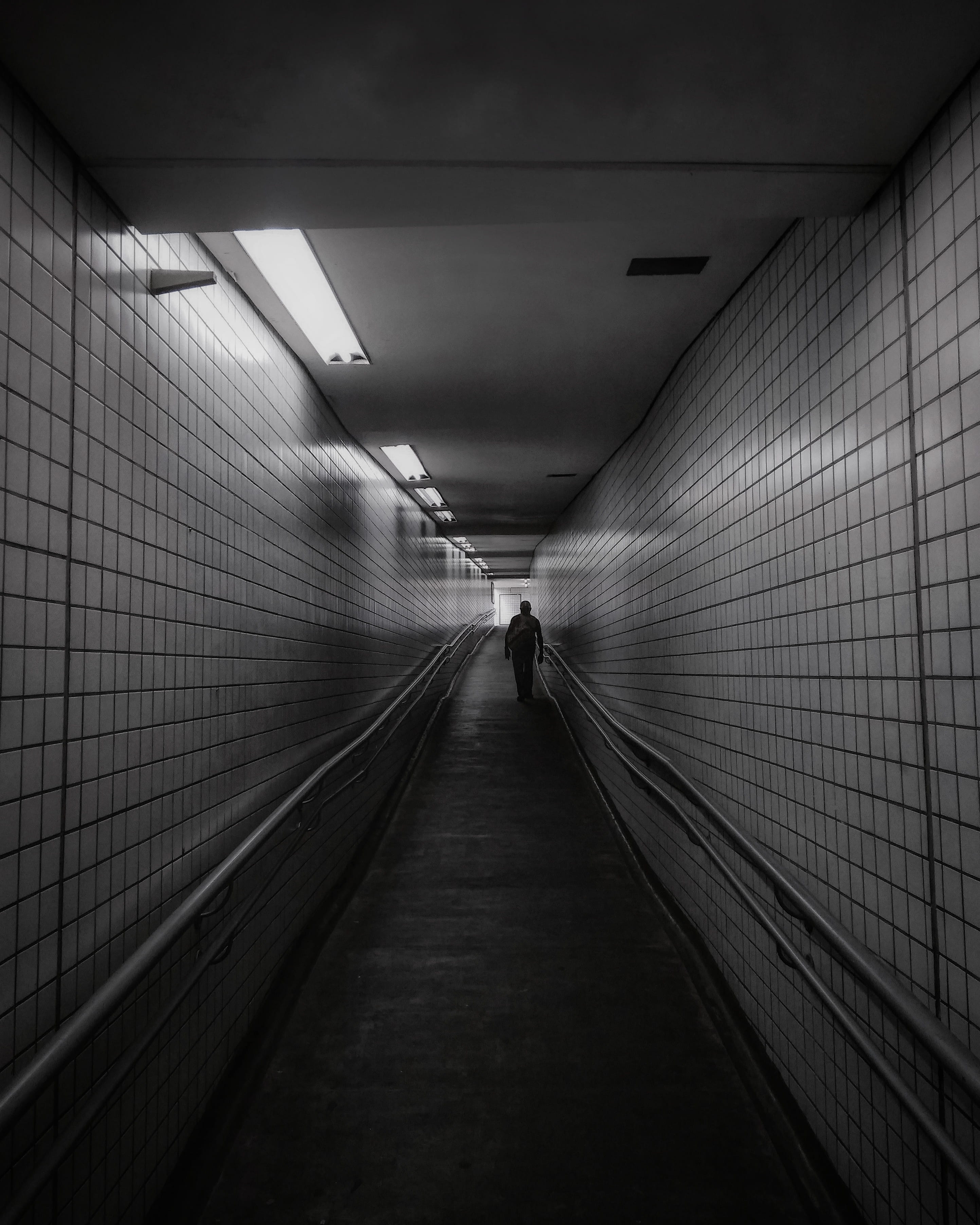 subway system, 2K, one person, dark, walking, underpass, underground walkway, building, flooring, lighting equipment, illuminated, black and white, diminishing perspective, Phone HD Wallpaper