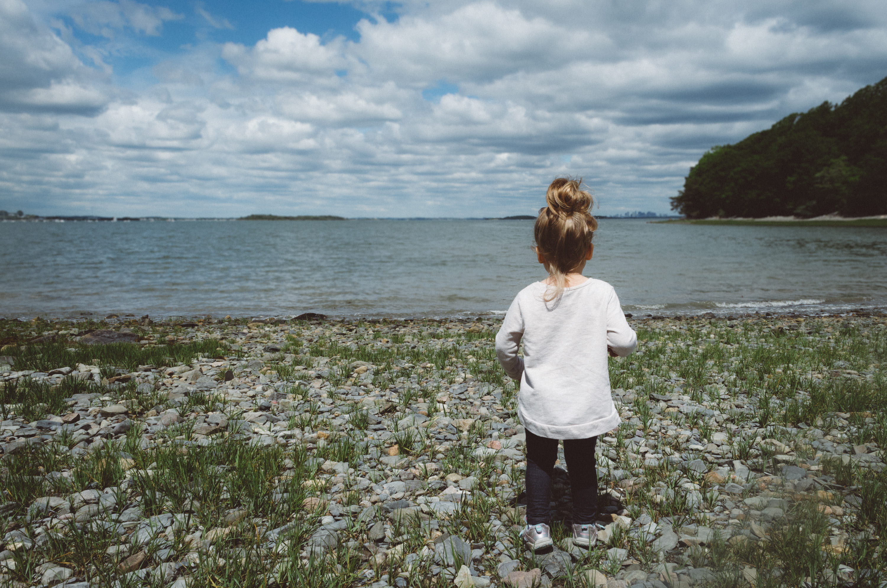 toddler, grass, casual clothing, looking at view, lake, beach, 2K, stones, cloud - sky, coast, standing, land, female, nature, seashore, day, photography, HD Wallpaper