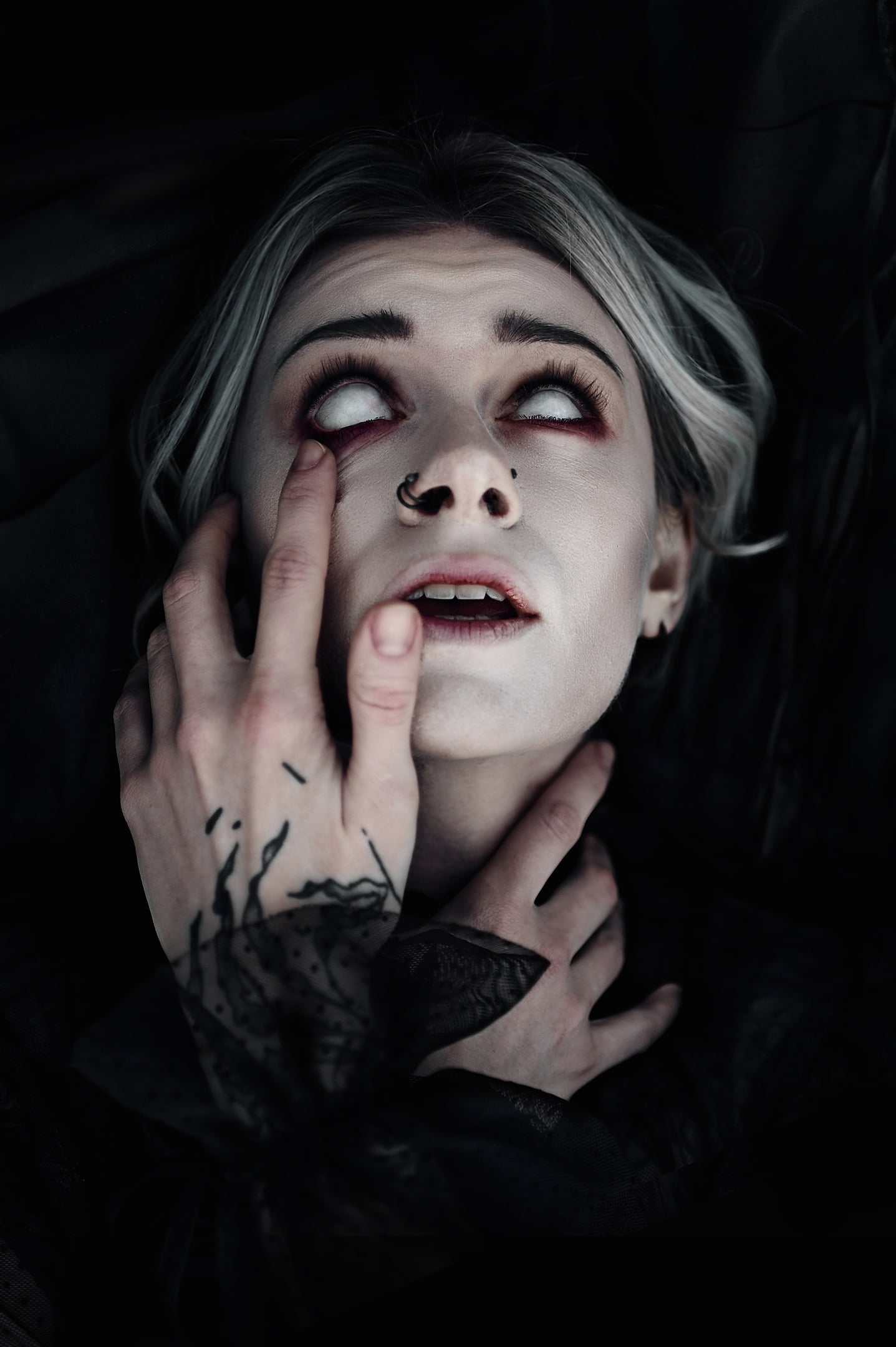 blonde, black background, 1080P, vertical, looking up, tattoo, dyed hair, touching face, dark background, pierced nose, black clothing, white eyes, model, Phone HD Wallpaper