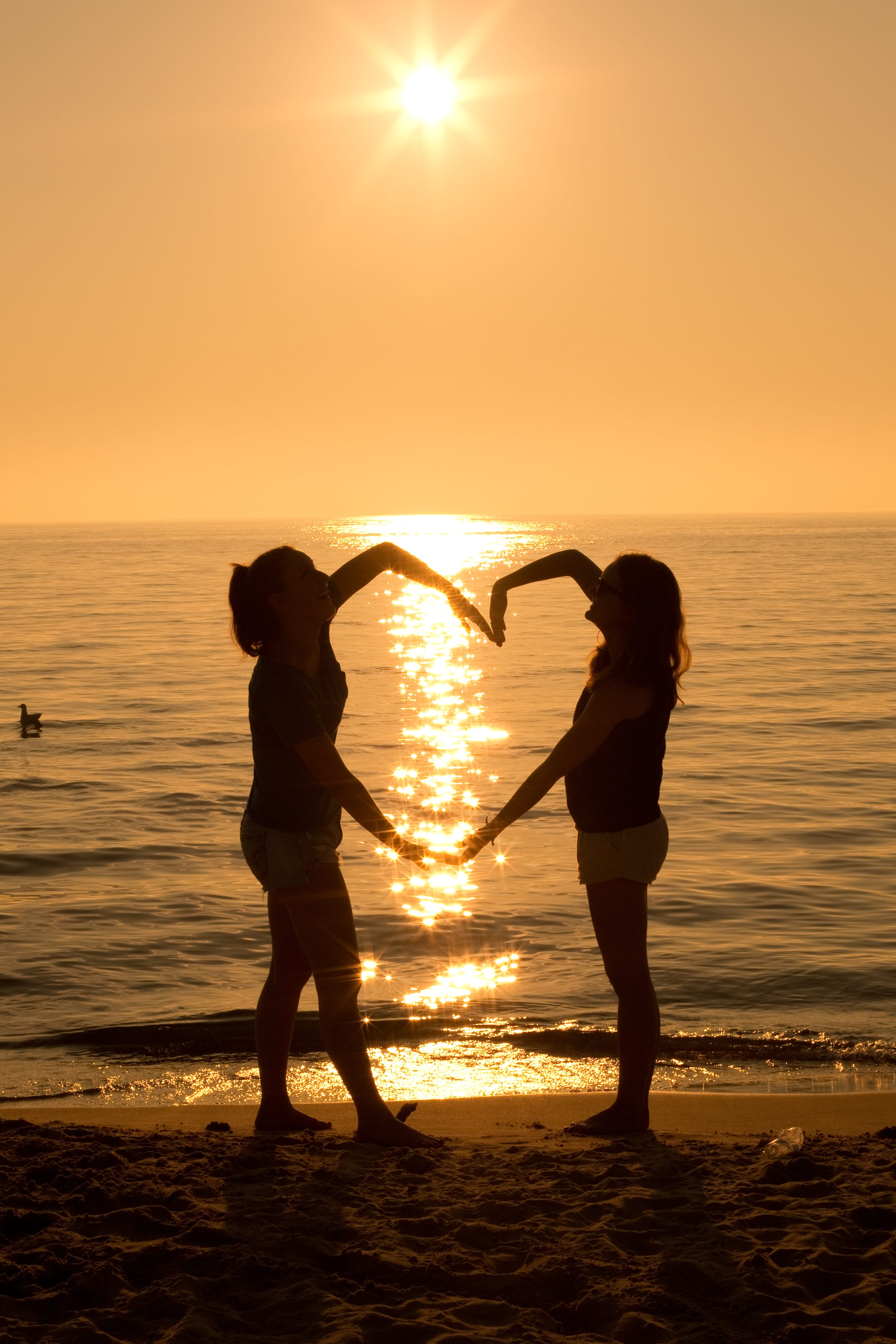 real people, horizon over water, beauty in nature, lens flare, lifestyles, hour, sea, silhouette, heart, women, sky, beach, standing, horizon, sun, two, Phone HD Wallpaper