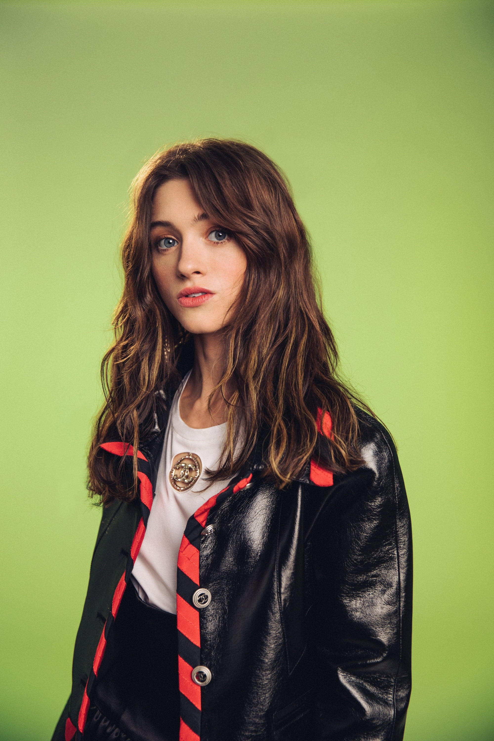 Natalia Dyer, blue eyes, actress, green background, 2K, black jackets, women, long hair, brunette, Phone HD Wallpaper