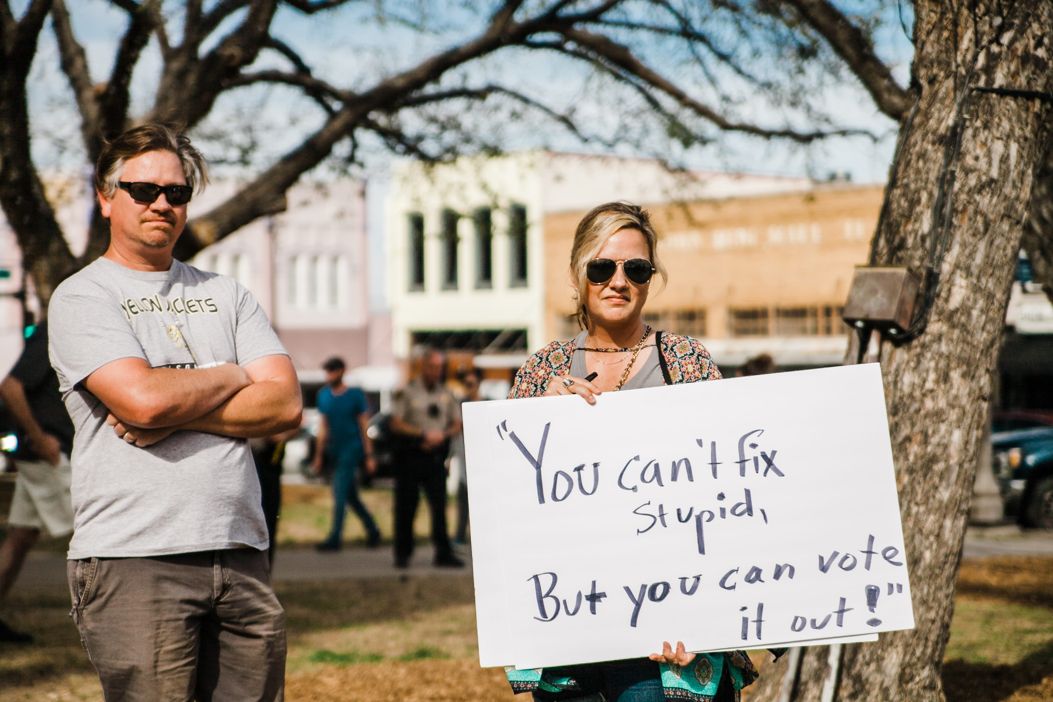 communication, nature, sign, board, holding, signage, buy, print, man, adult, can, standing, portrait, wearing, stupid, woman, text, white, tree, focus on foreground, HD Wallpaper