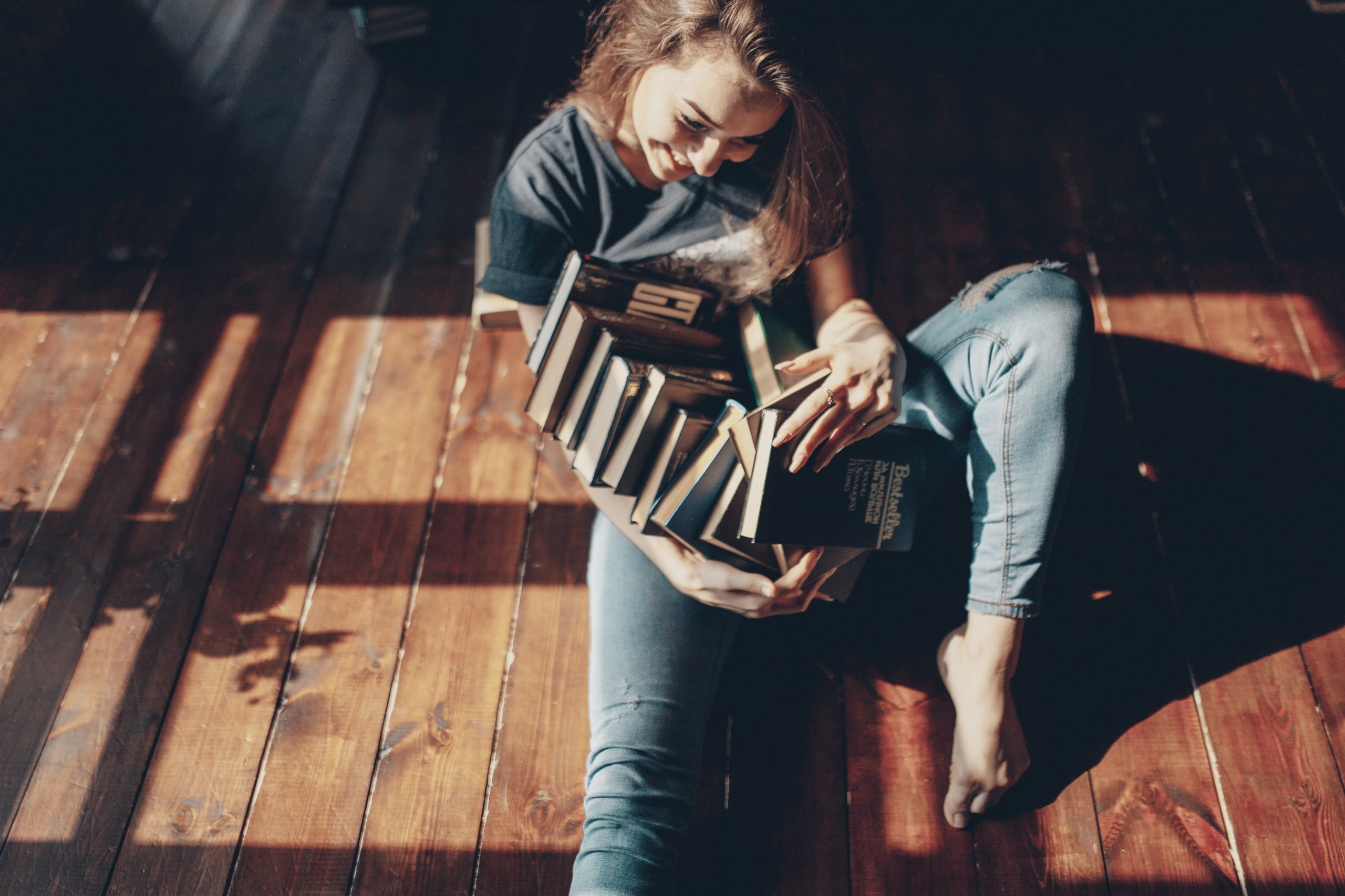brunette, women indoors, sun rays, sitting, barefoot, women, 2K, books, smiling, feet, torn jeans, on the floor, model, T-shirt, HD Wallpaper