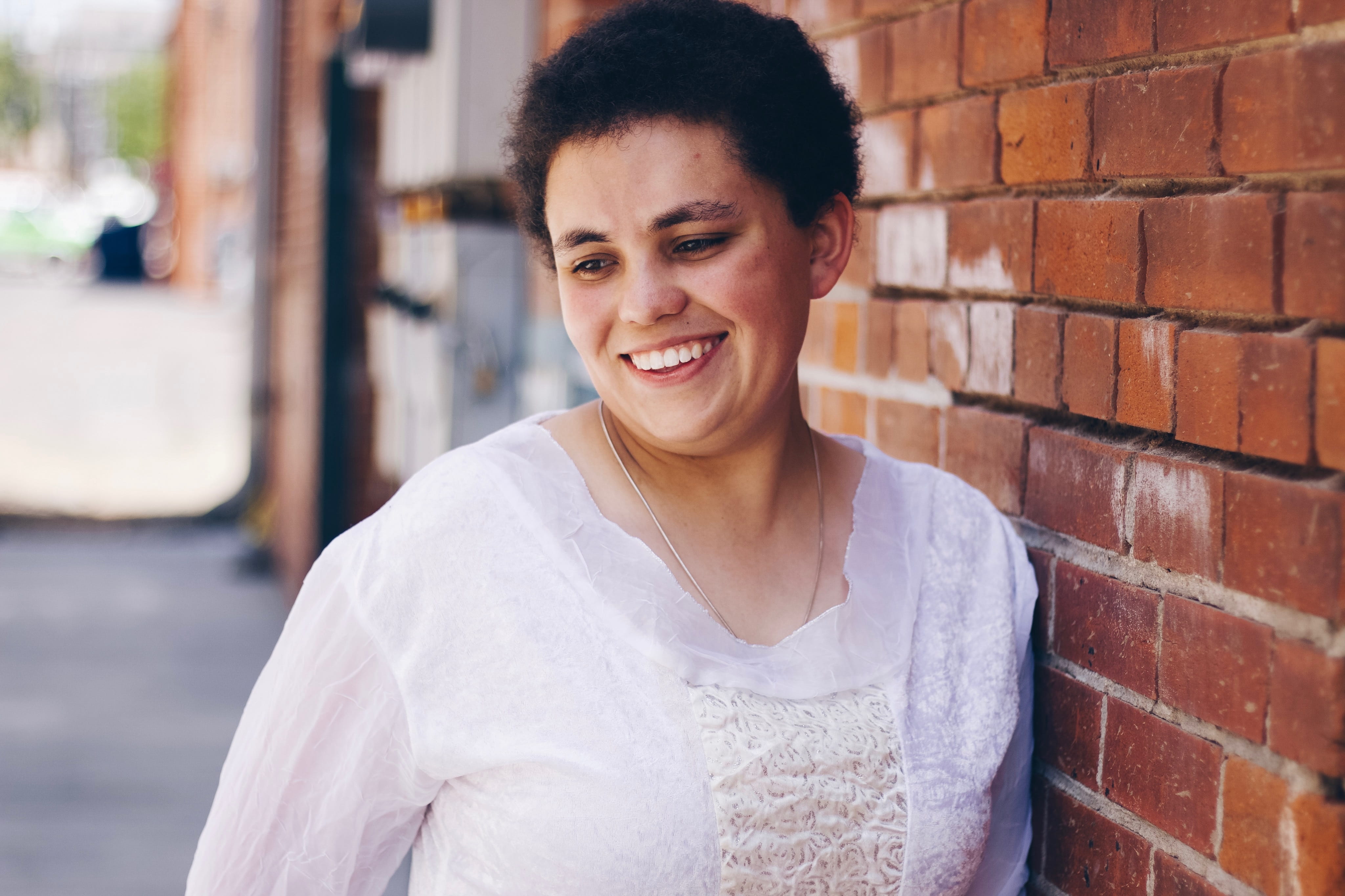 front view, outdoors, smiling, people, one person, woman, happiness, portrait, brick wall, denver, person, architecture, short hair, leaning, happy, wall, HD Wallpaper