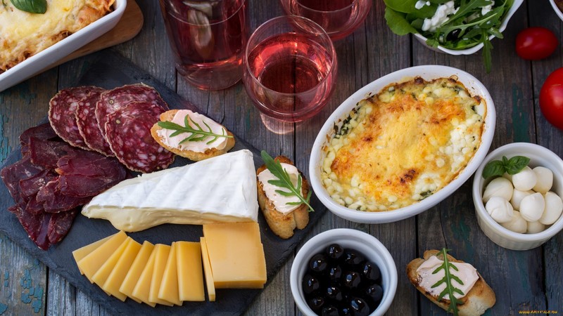 food, cheese, sausage, olives, salad, cutting board, charcuterie board, wine, wine glass, basil, tomatoes, bread, pepperoni, wooden surface, top view