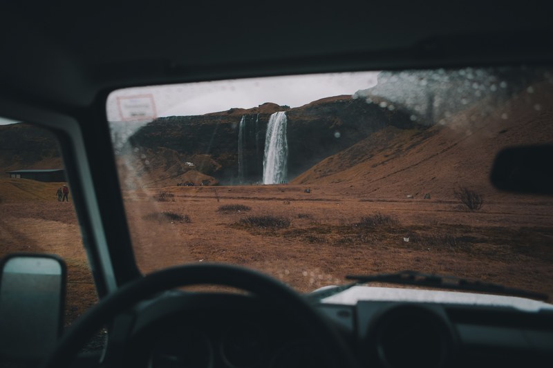 a view through a windshield on a waterfall surrounded by tourists in cold plains, seljalandsfoss 4k