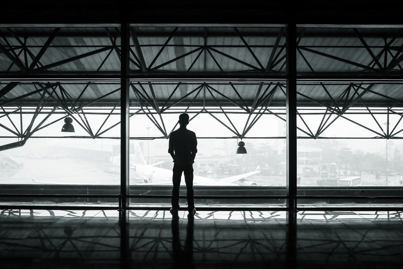 a silhouetted man looks at a plane out an airport window, man looks out airport window 4k