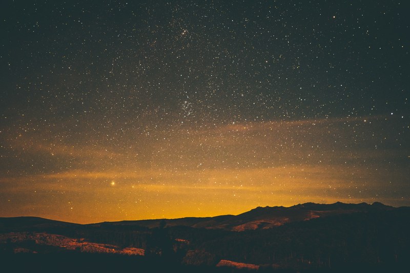 a golden sunset fades into a dark starry night sky over some mountains, stars over the mountain 4k