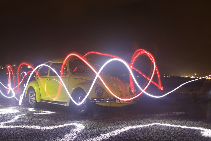 red and white light trails drawn in the air in front of the yellow vintage volkswagen beetle at night, light trails in front of volkswagen beetle 4k