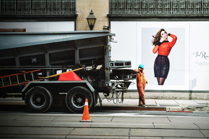 a construction worker stands alongside a truck with a wall of advertisements behind him, construction worker and ad 4k