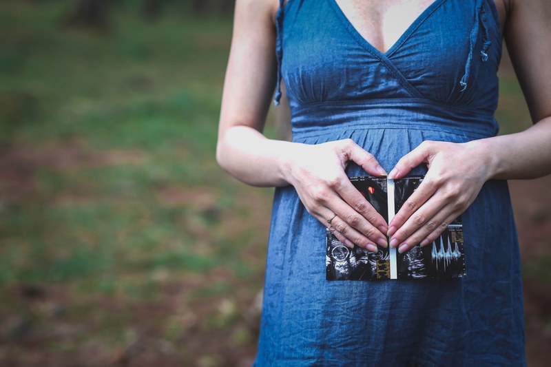 a pregnant woman holding an ultrasound picture against her stomach and making a heart shape with her fingers, waiting for an angel 4k