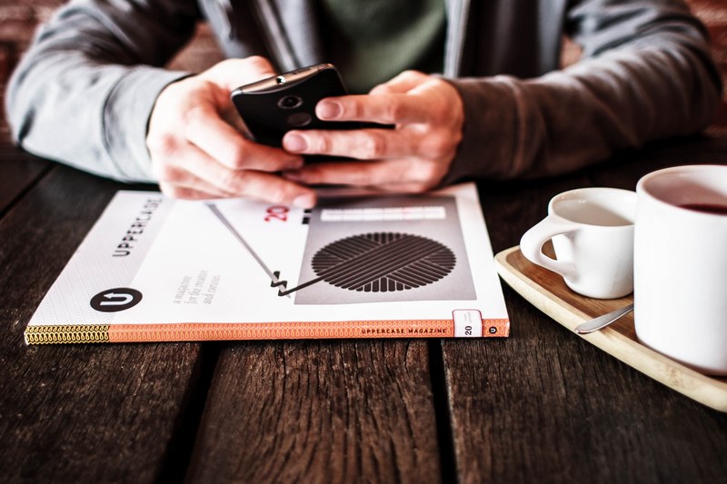 a person in a hoodie using a phone at a table over coffee, smartphone and coffee 4k
