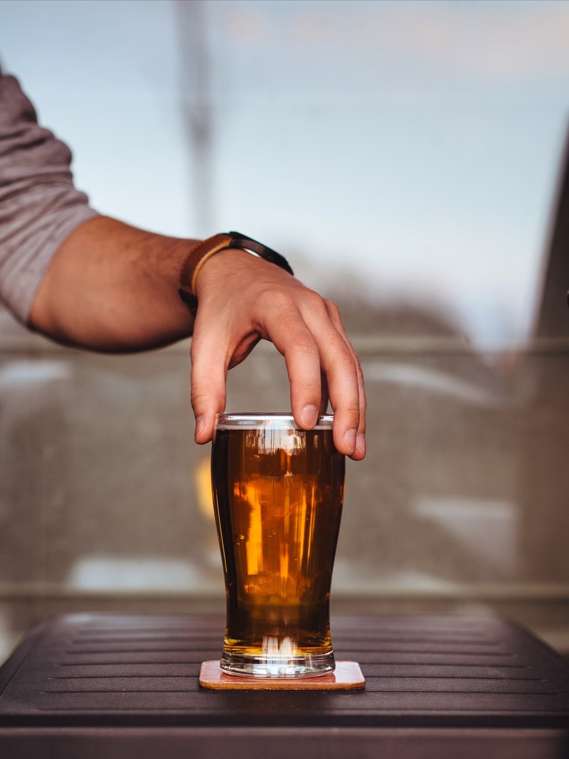 a man with a rolled up sleeve holding the tip of a glass cup of beer relaxing, man holding glass of beer 4k