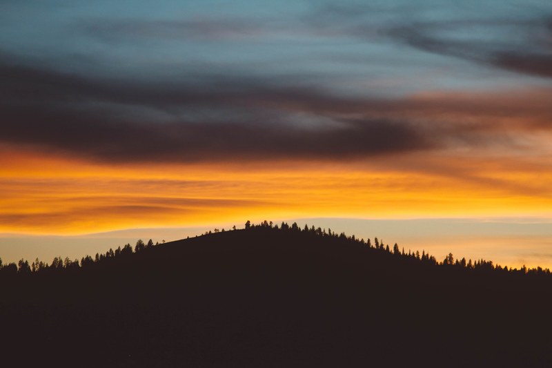 a silhouette of a wooded hill against orange sky during sunset, dark hill under fiery sky 4k