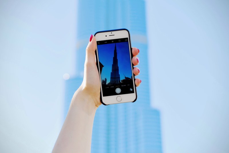 a womans hand holding an iphone with its camera pointed at burj khalifa in dubai, photographing burj khalifa 4k