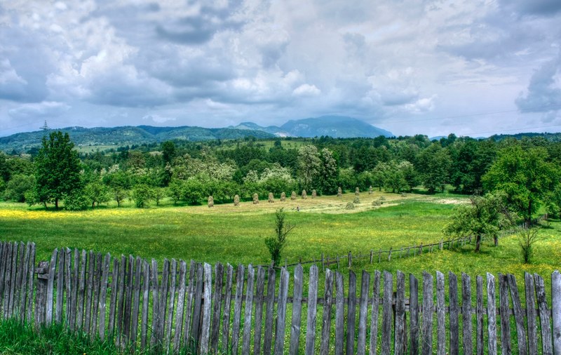 a wooden fence enclosing a meadow with heaps of hay in soveja, rustic fence by a meadow 4k