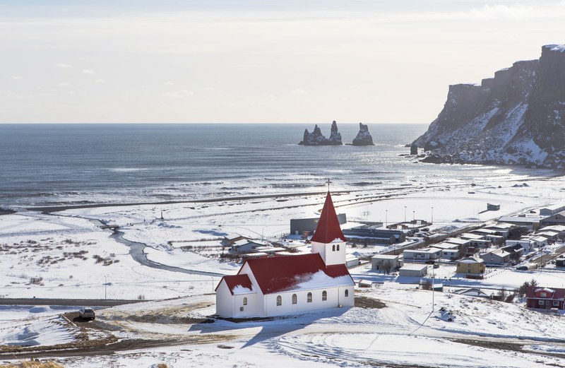 drone shot of a white church with dark red roof next to a small village near a lake, a village church in winter 4k