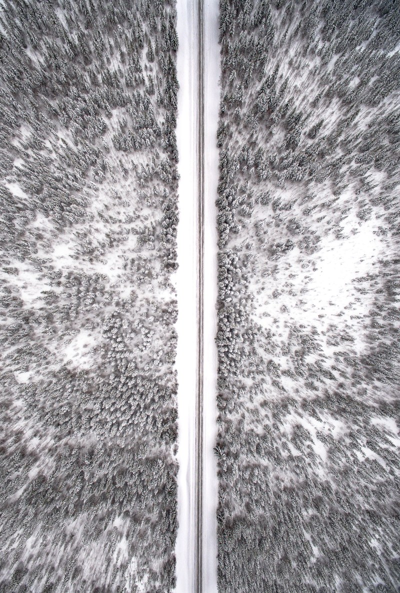 a drone shot of a narrow road cutting through a snowy forest in jamtland county, long snowy road from above 4k